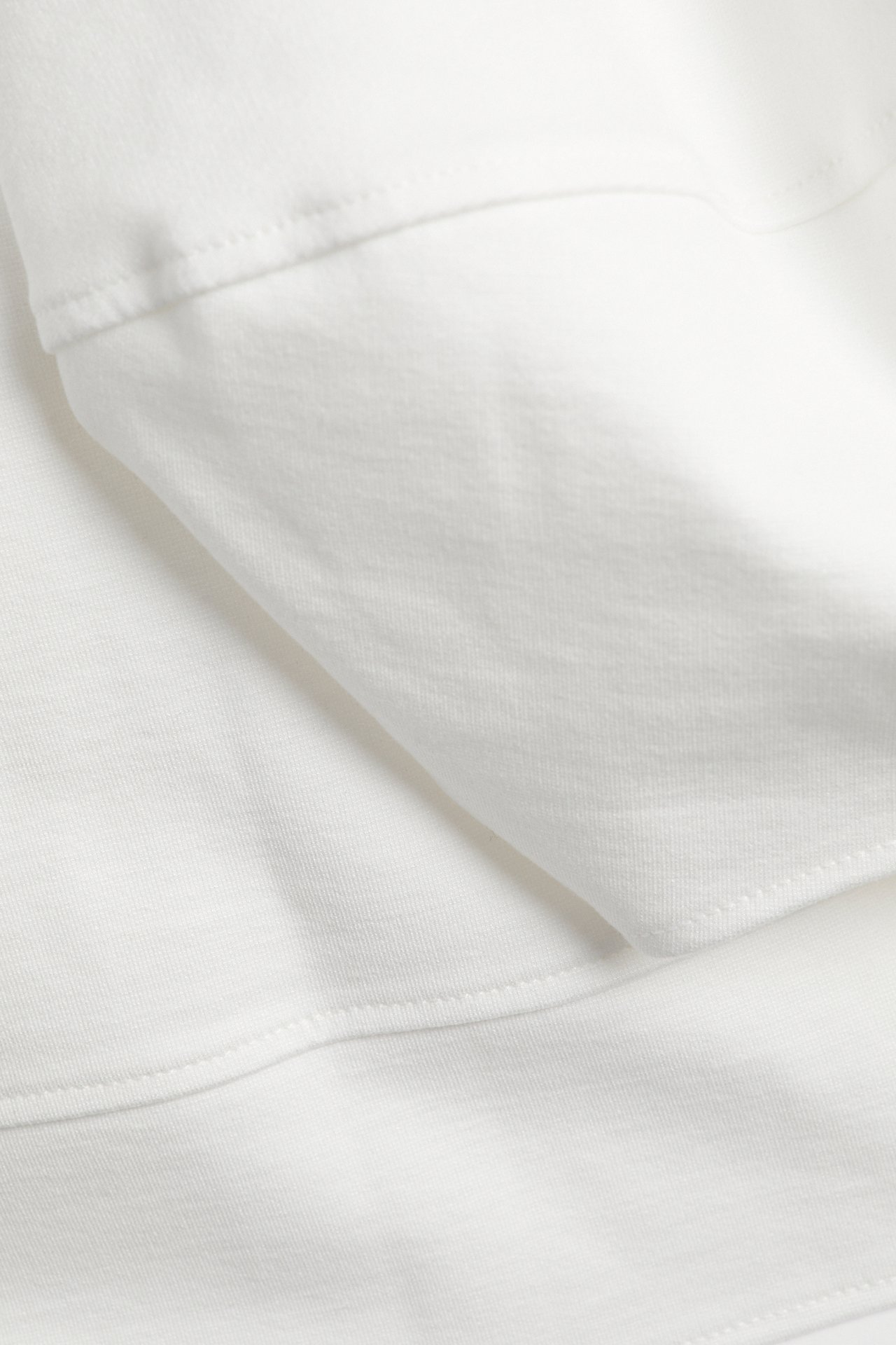 Närbild av en offwhite punto-topp, som visar den släta tygstrukturen och sydda sömmar.
