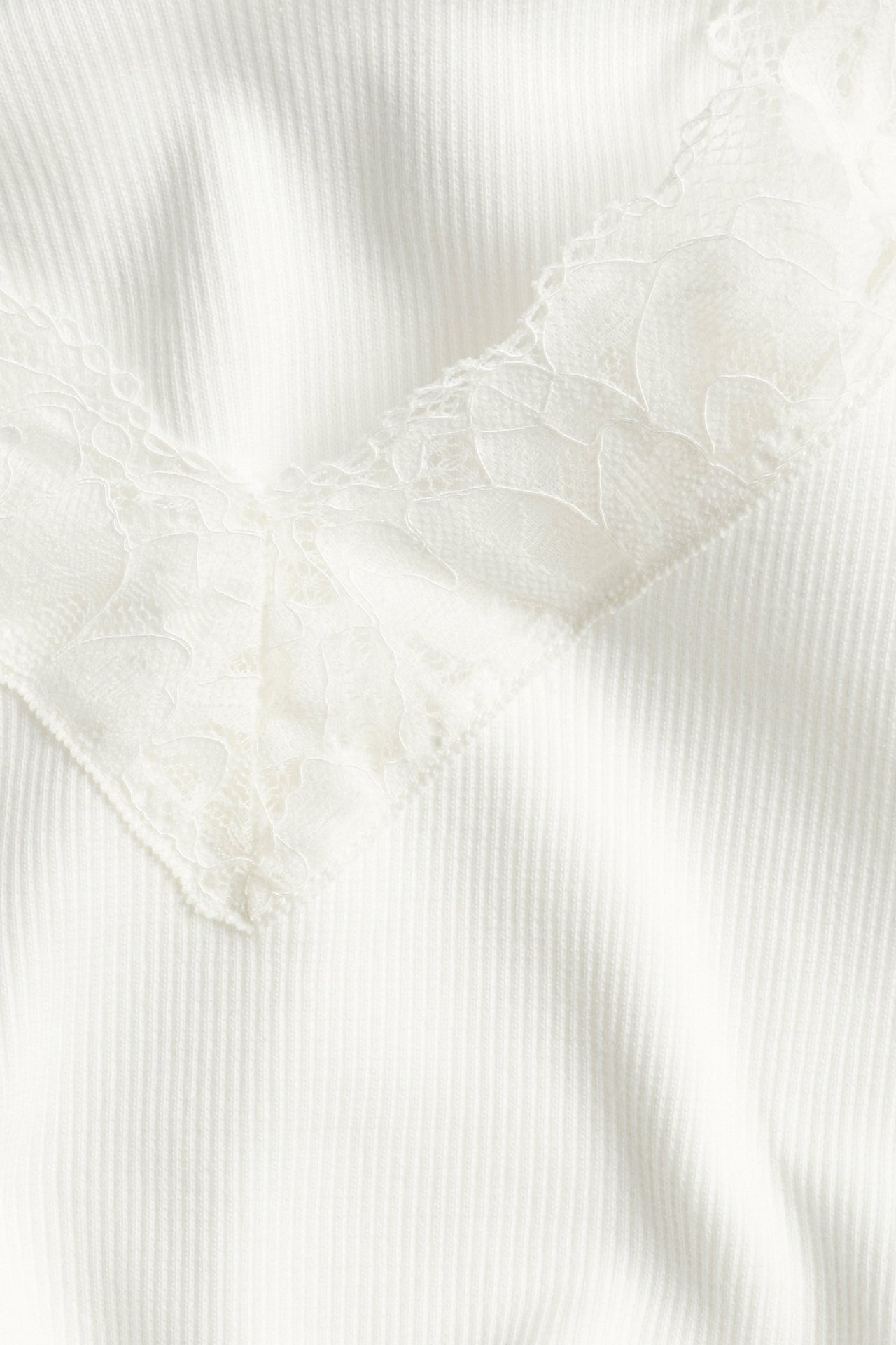 Zbliżenie na kremowy prążkowany top z długim rękawem, dekoltem w serek i koronkową lamówką.