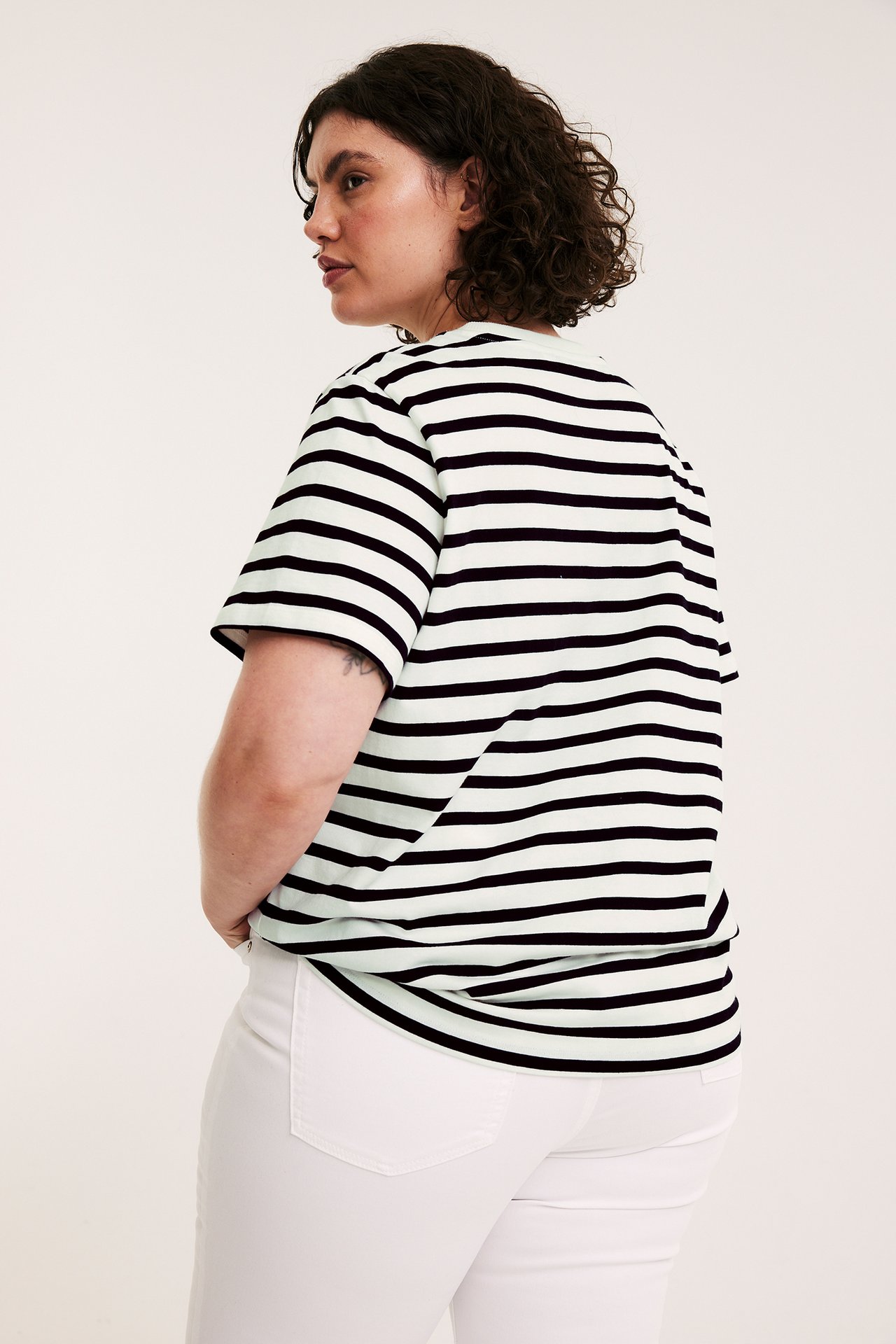 Sida bakifrån av kvinna i svart och mintgrön randig kortärmad topp och vita byxor.