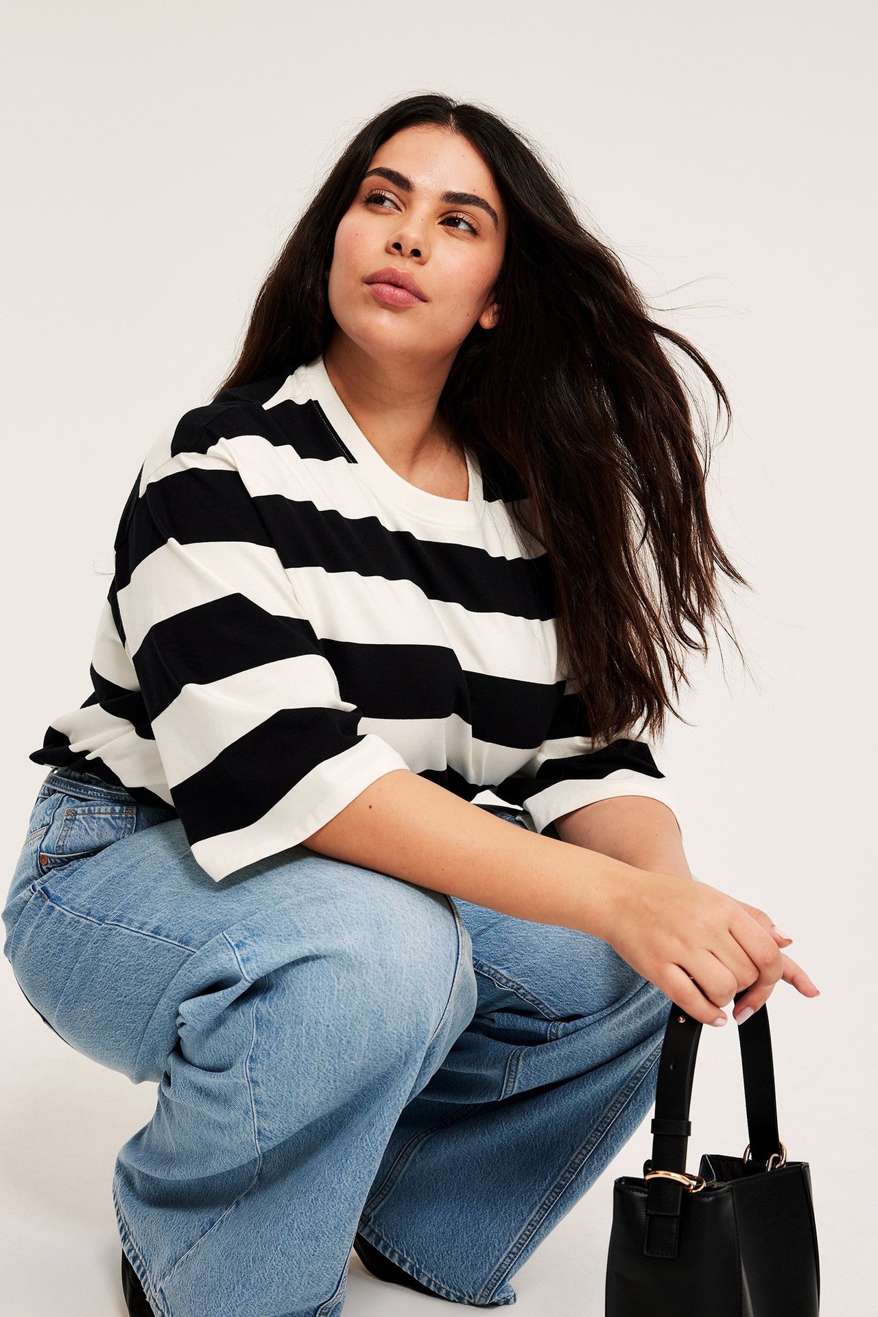 Etunäkymä: Nainen raidallisessa offwhite ja musta oversized puuvilla-t-paidassa, vaaleansiniset farkut, musta laukku.