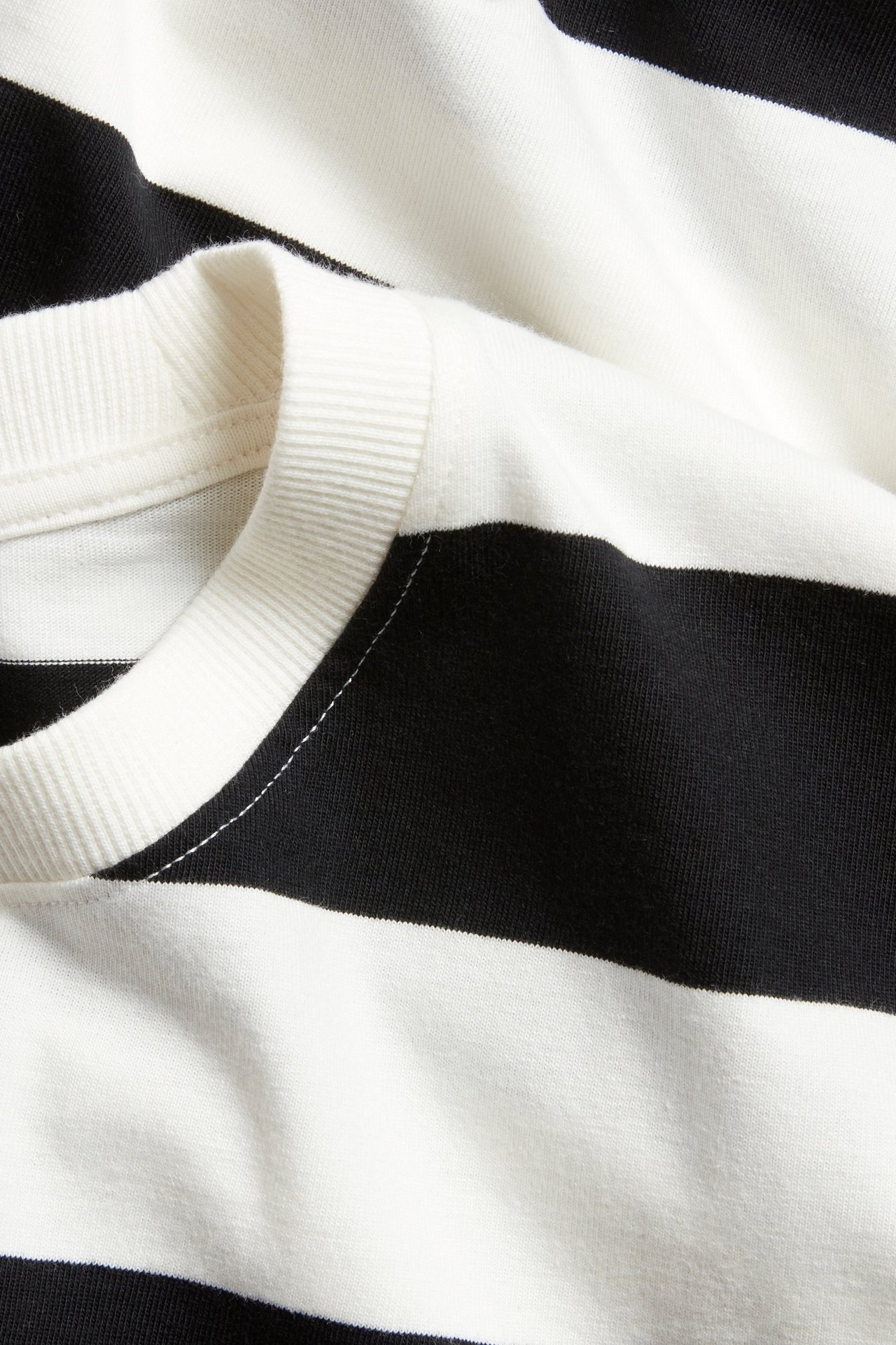 Zbliżenie czarno-białego bawełnianego t-shirtu oversize w paski z prążkowanym dekoltem.