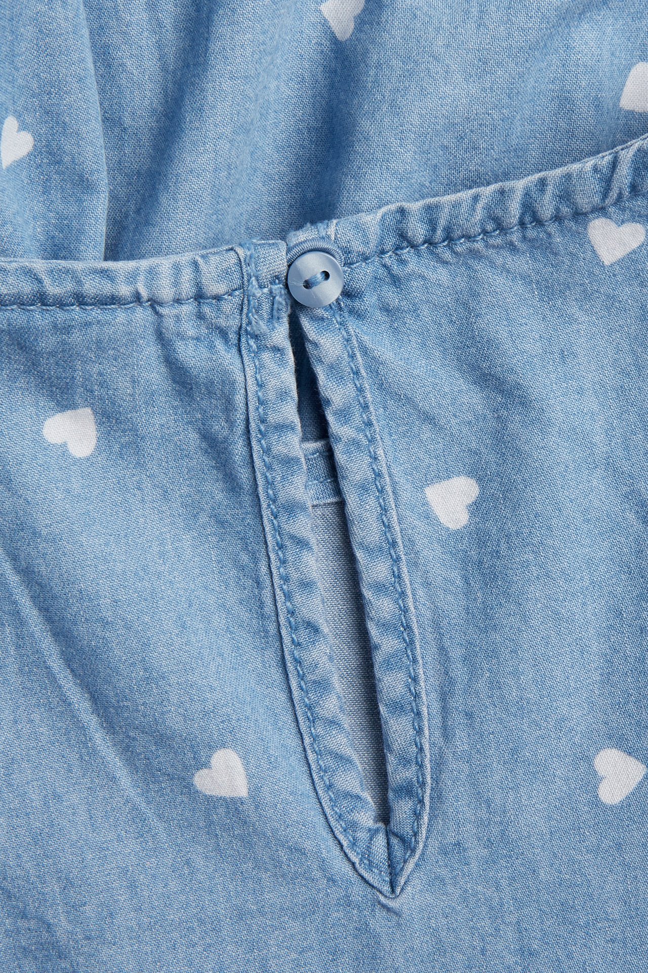 Zbliżenie na dziecięcą jasnoniebieską bluzkę dżinsową z białymi sercami i zapięciem na guzik z tyłu.