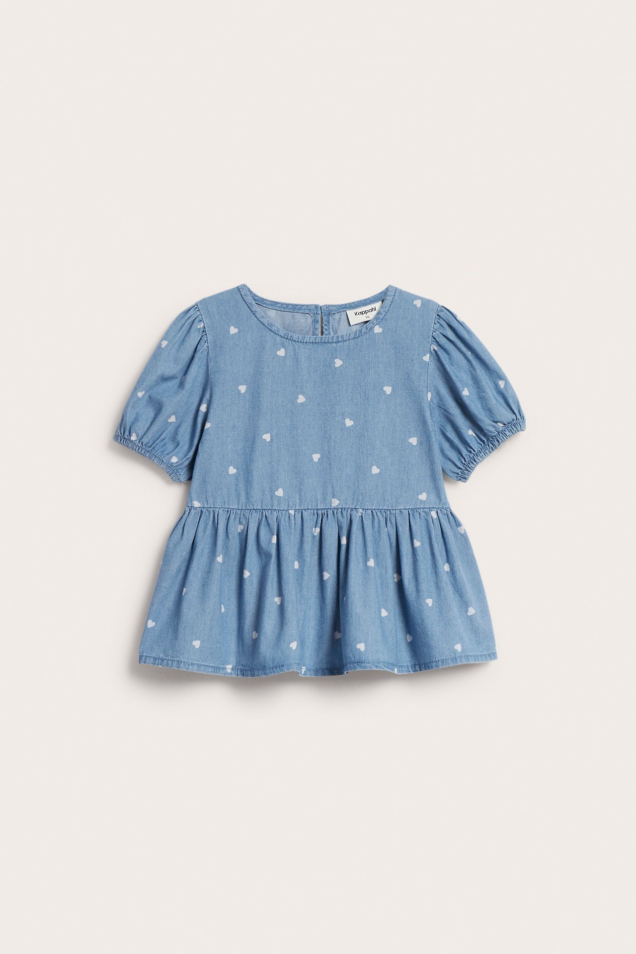 Forfra, en lys denim barnebluse med hjertemønster, puffermer, elastiske mansjetter og peplum-kant.