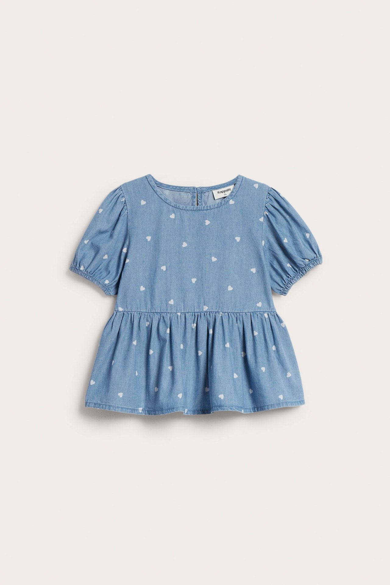 Framifrån, en ljus denim barnblus med hjärtmönster, puffärmar, elastiska ärmslut och peplum-fåll.