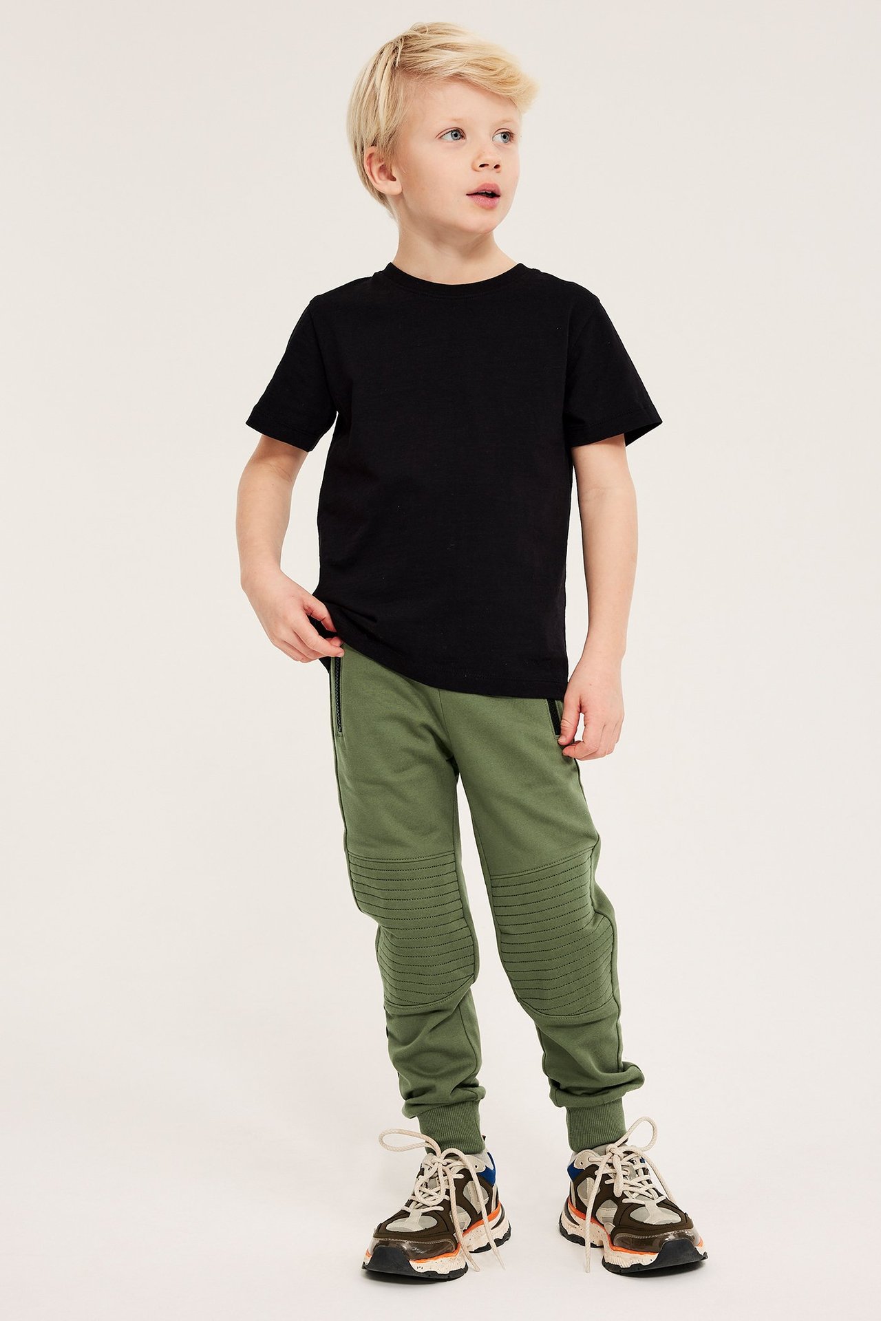 Frontbilde av barn i mørkegrønne bomullsjoggebukser med forsterkede knær og en svart t-skjorte.