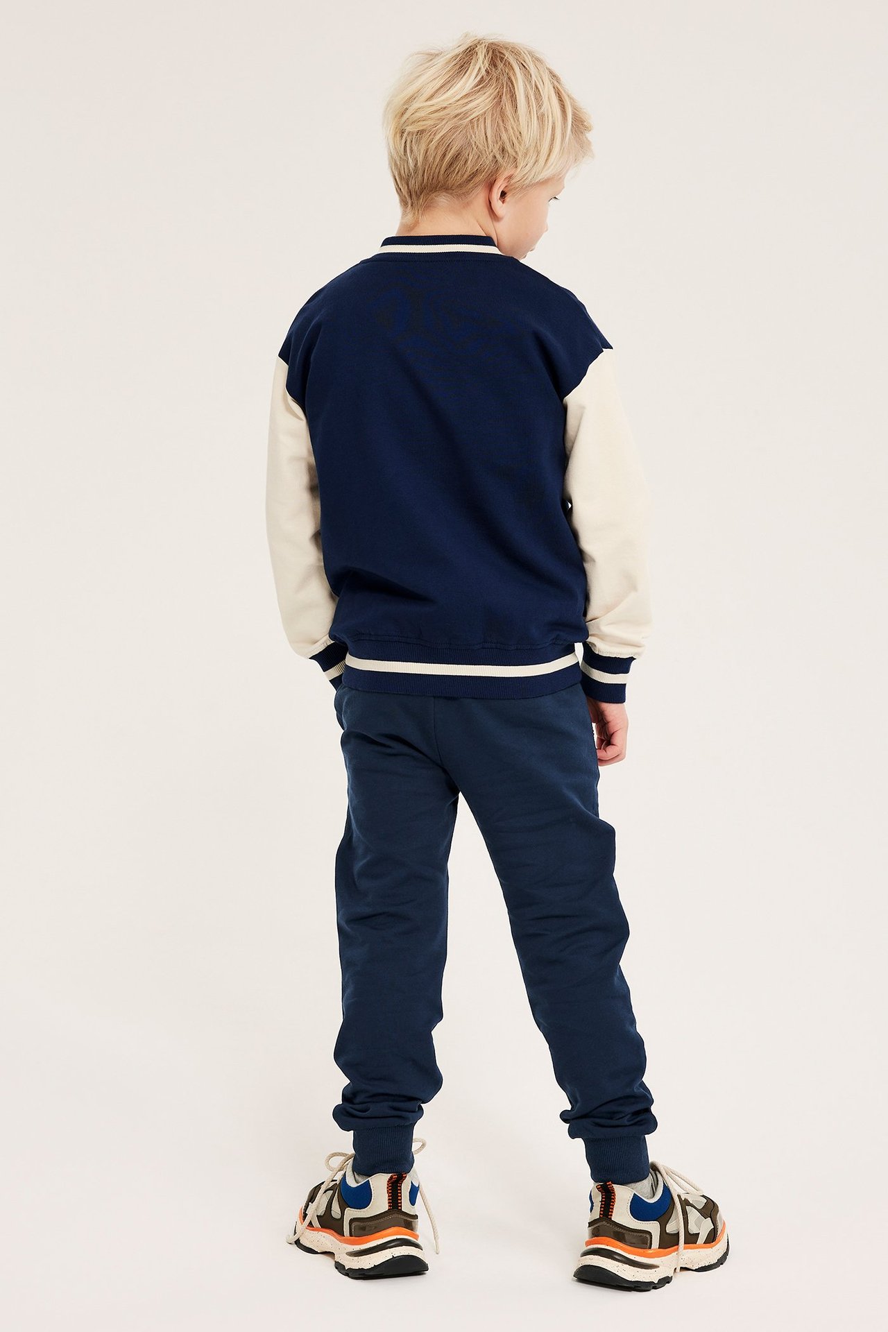 Bakfra: et barn i mørkeblå joggebukse, en tofarget collegejakke og joggesko.