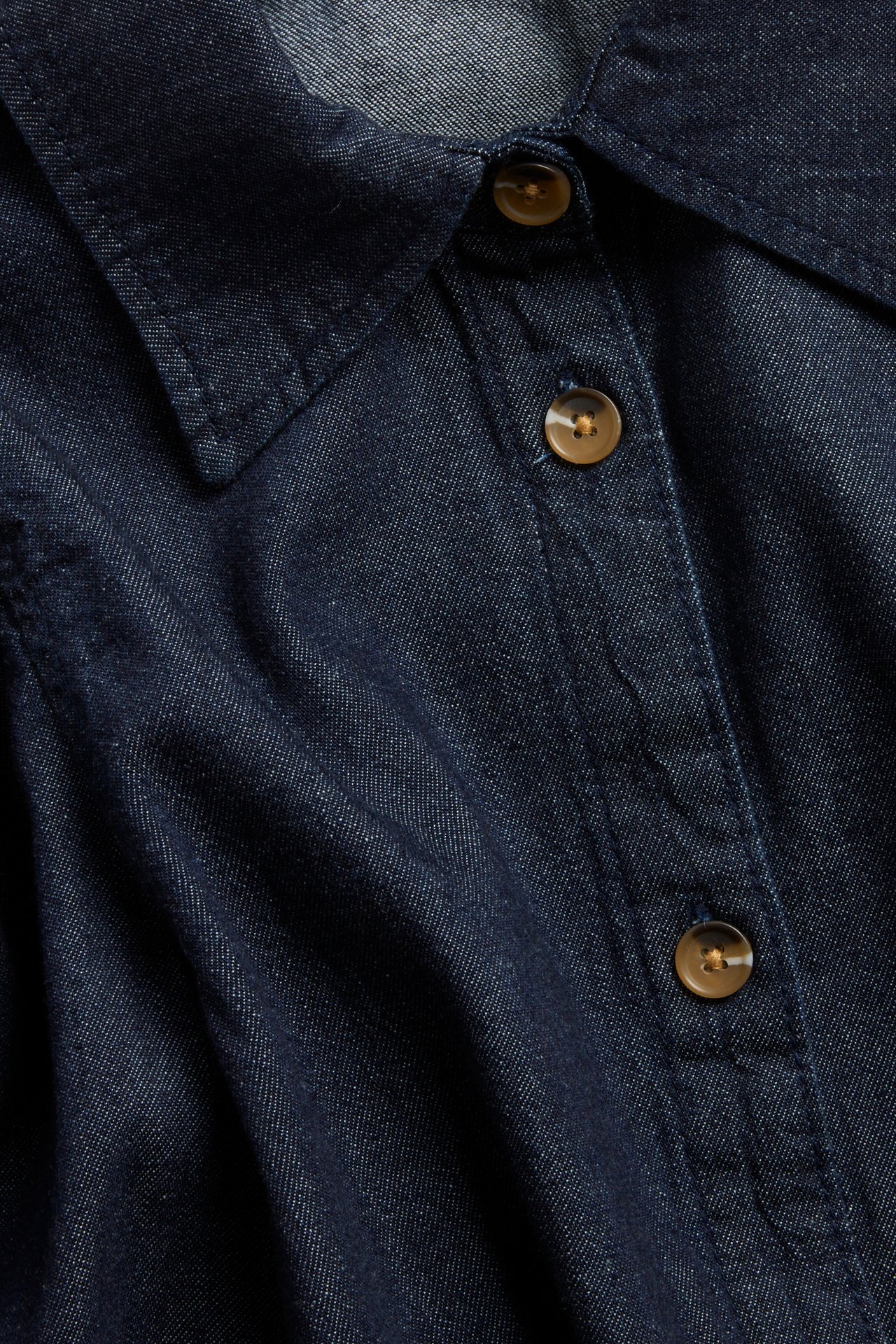 Lähikuva tummasta denimbluusista, jossa on kaulus ja nappilista sarvinapilla.