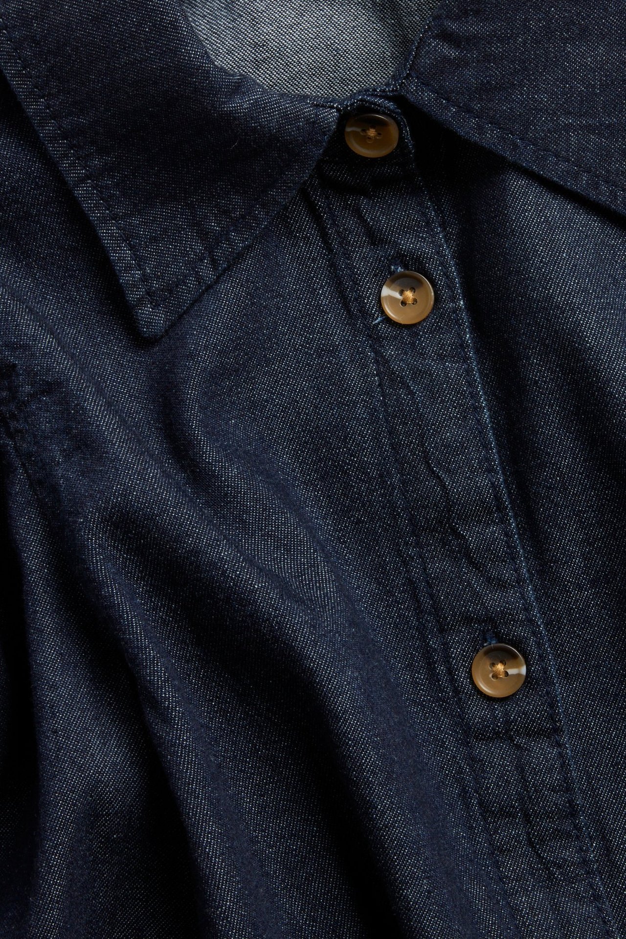 Zbliżenie ciemnej bluzki dżinsowej z kołnierzem i guzikami imitującymi róg na plisie.