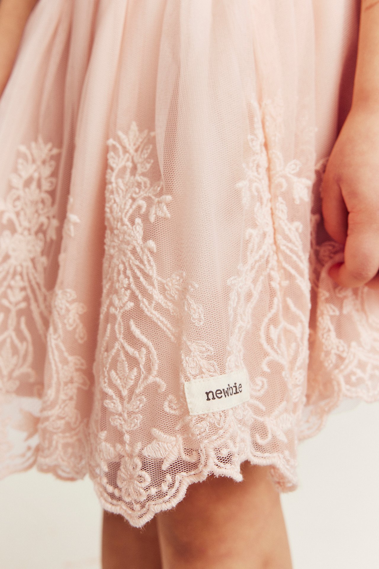 Lähikuva edestä lapsen vaaleanpunaisesta brodeeratusta verkkohameesta, jossa 'newbie'-etiketti.