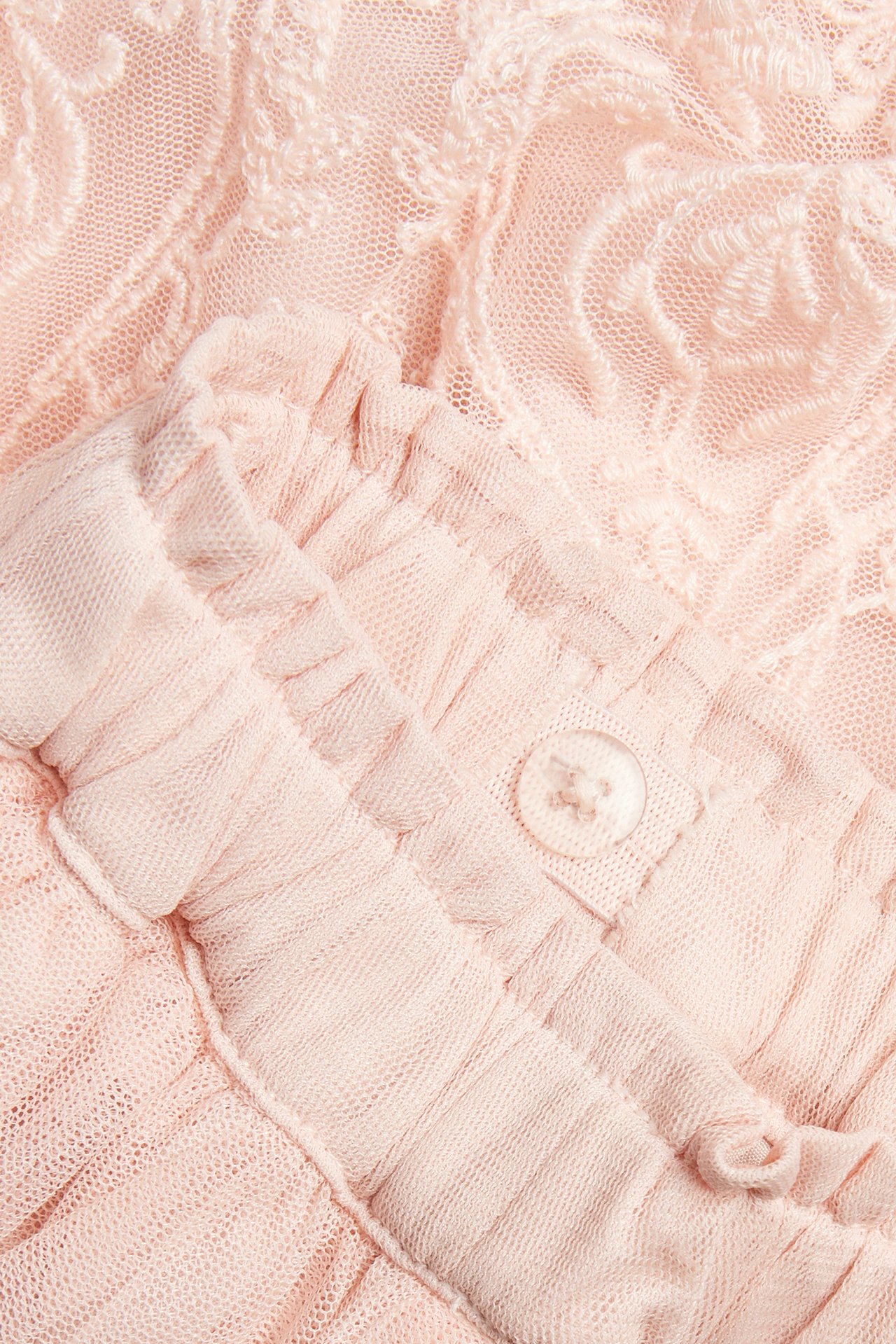 Lähikuva vaaleanpunaisesta brodeeratusta verkkohameesta, jossa röyhelöitä ja nappi.