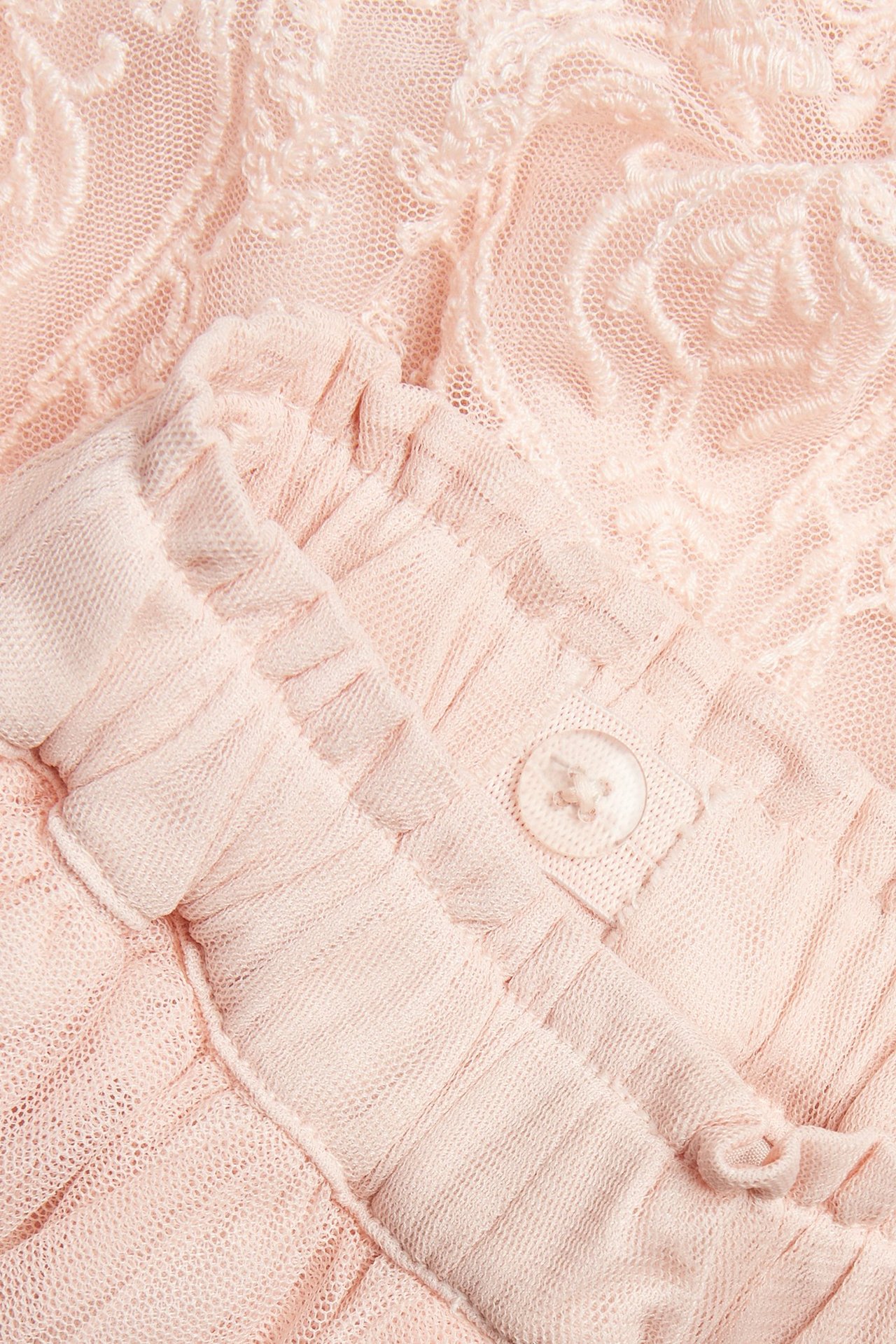 Zbliżenie na jasnoróżową haftowaną spódnicę z siateczki z falbankami i guzikiem.