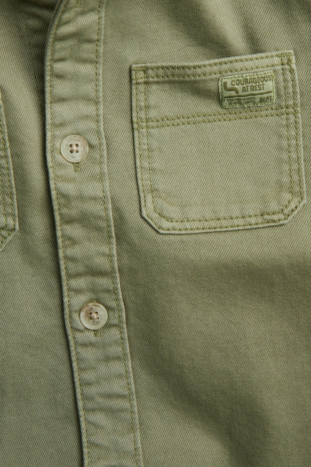 Zbliżenie na ciemnozieloną, jednolitą koszulę z twillu bawełnianego z guzikami i kieszenią z naszywką.