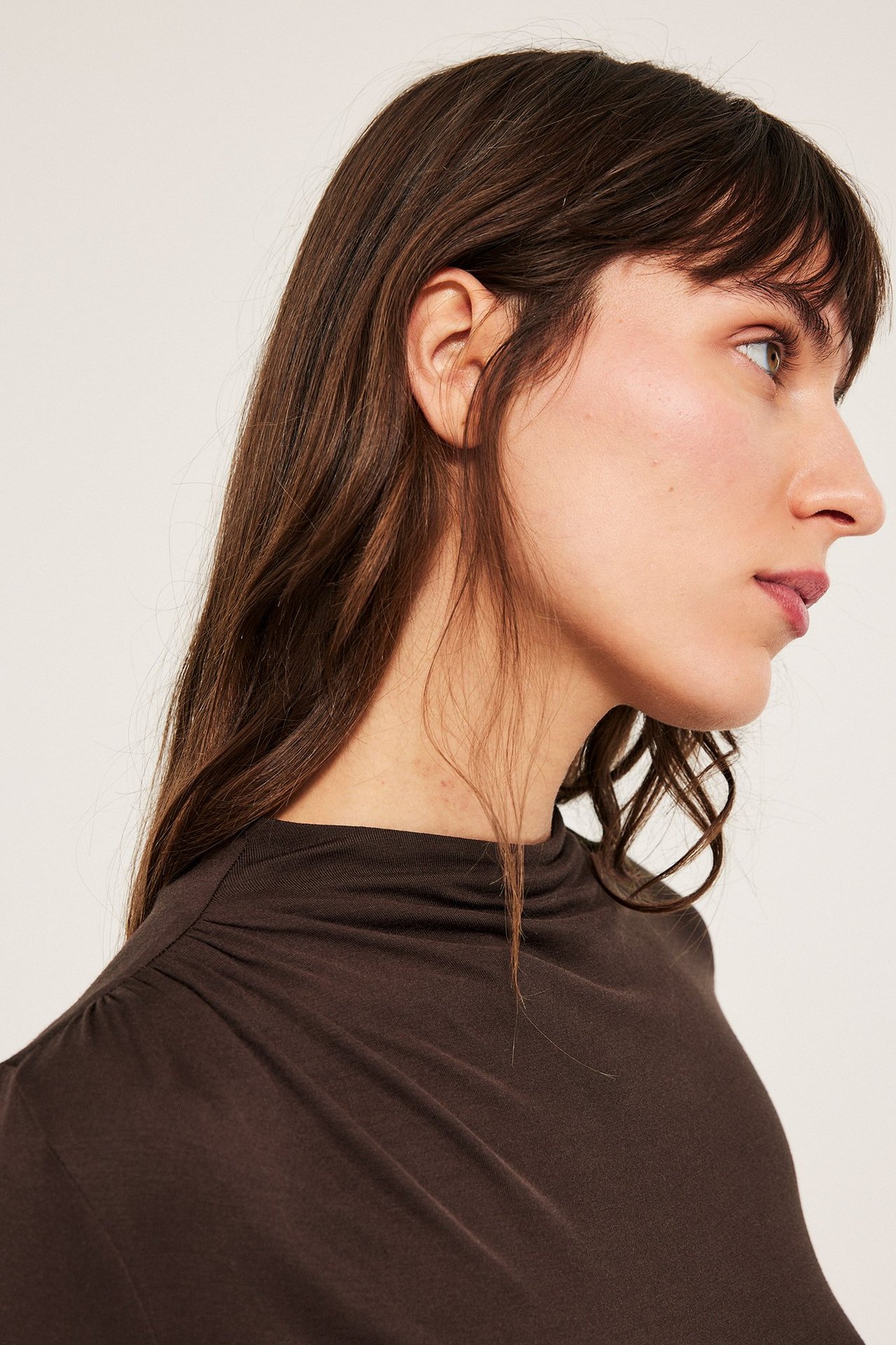 Modelka w profilu w ciemnobrązowej długoskrętnieviskos top z draperią.