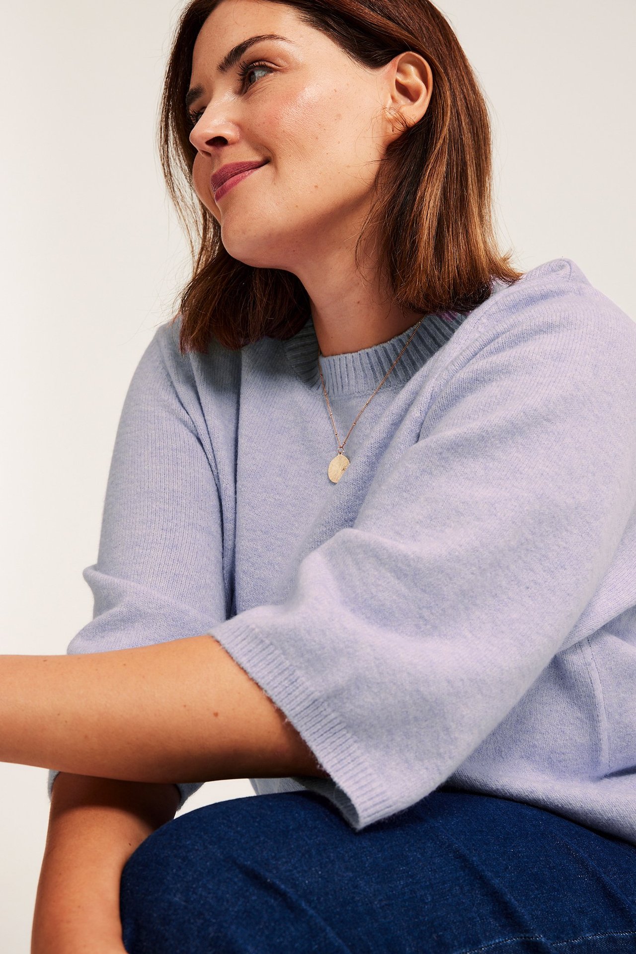 Lähikuva naisesta vaaleanlilassa 3/4-hihaisessa neulepaidassa ja kultaisessa kaulakorussa.