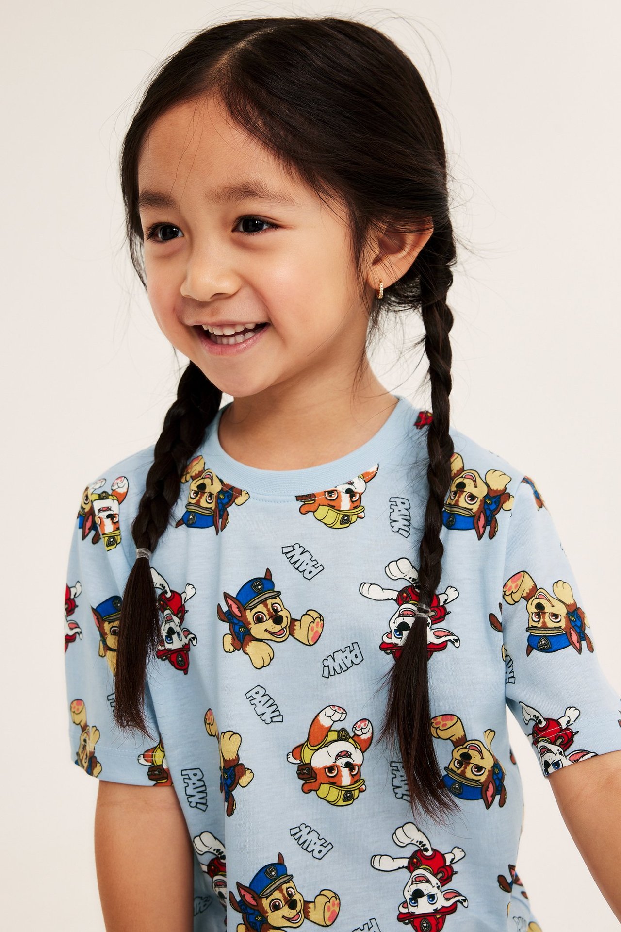 Närbild framifrån på leende barn i ljusblå kortärmad pyjamastopp i bomull med Paw Patrol-mönster.