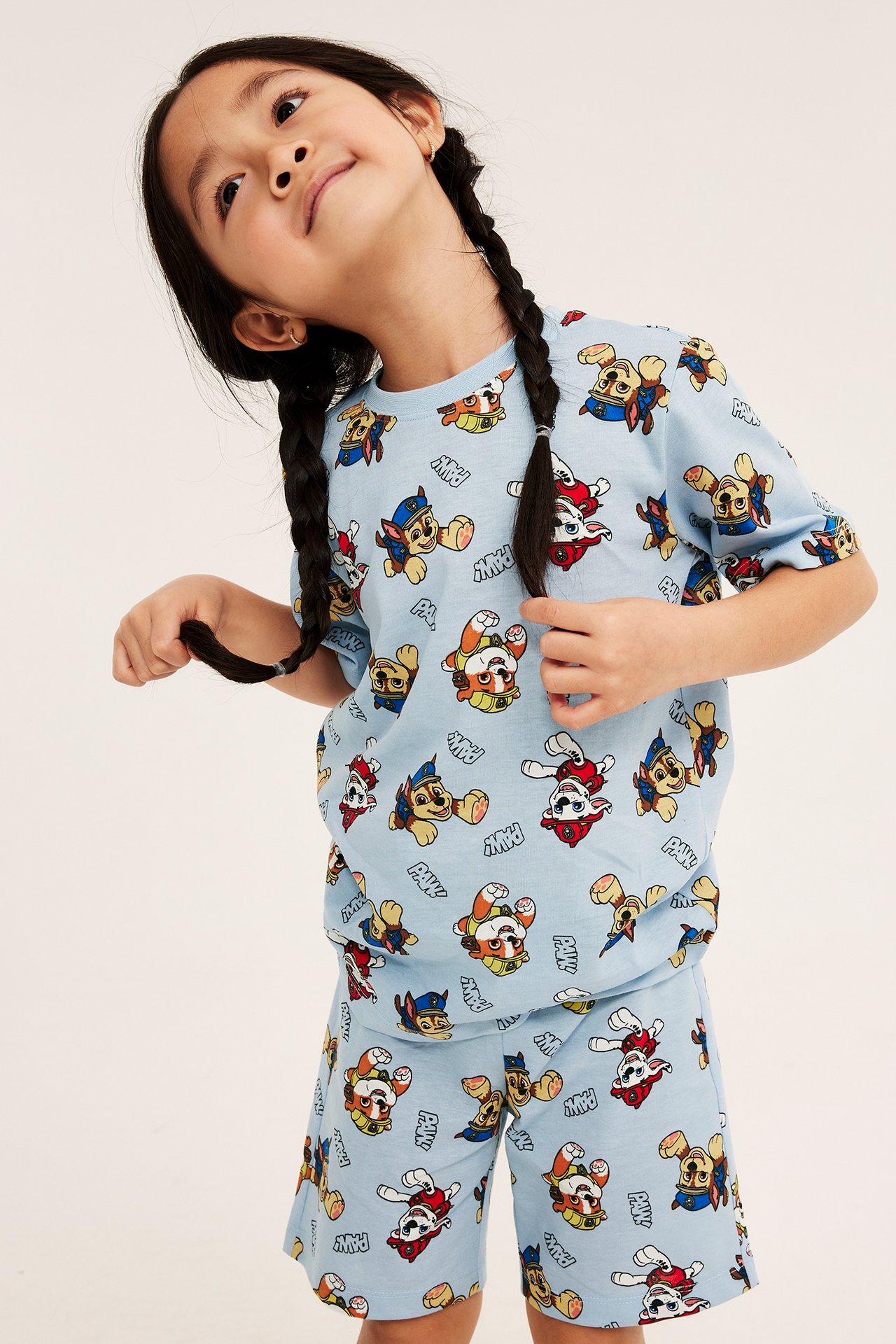 Ljusblå kortärmad pyjamas i bomull med heltäckande Paw Patrol-mönster, på ett barn. Framifrån.