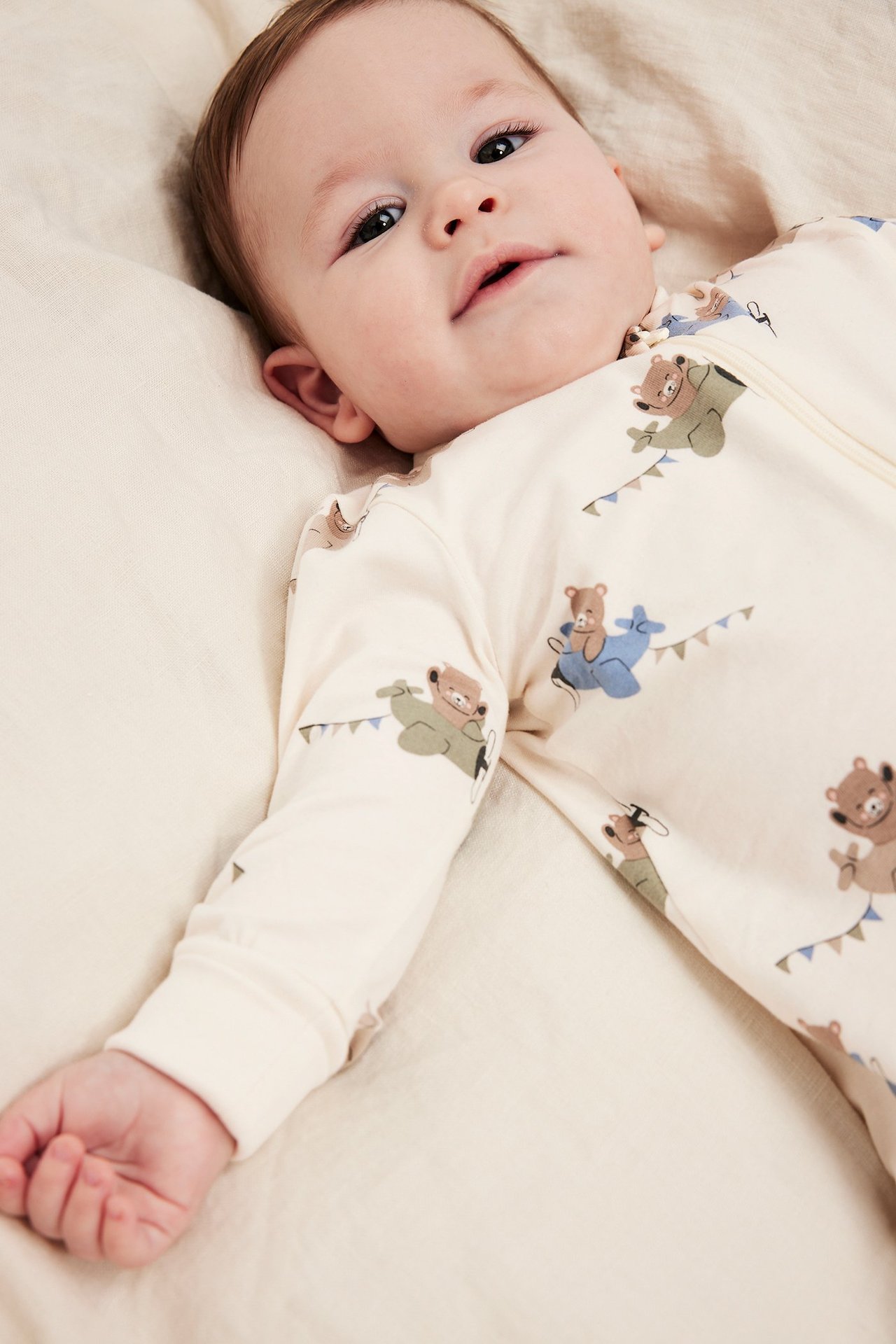 Nærbilde av en baby i offwhite bomullsromper med bjørn- og flymønster, toveis glidelås.