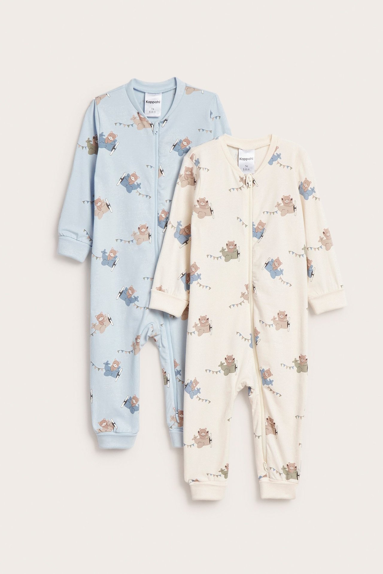 Edestä näkymä kahdesta vauvanpotkupuvusta: luonnonvalkoinen ja vaaleansininen, nallekuvioiset, kaksisuuntaisilla vetoketjuilla.