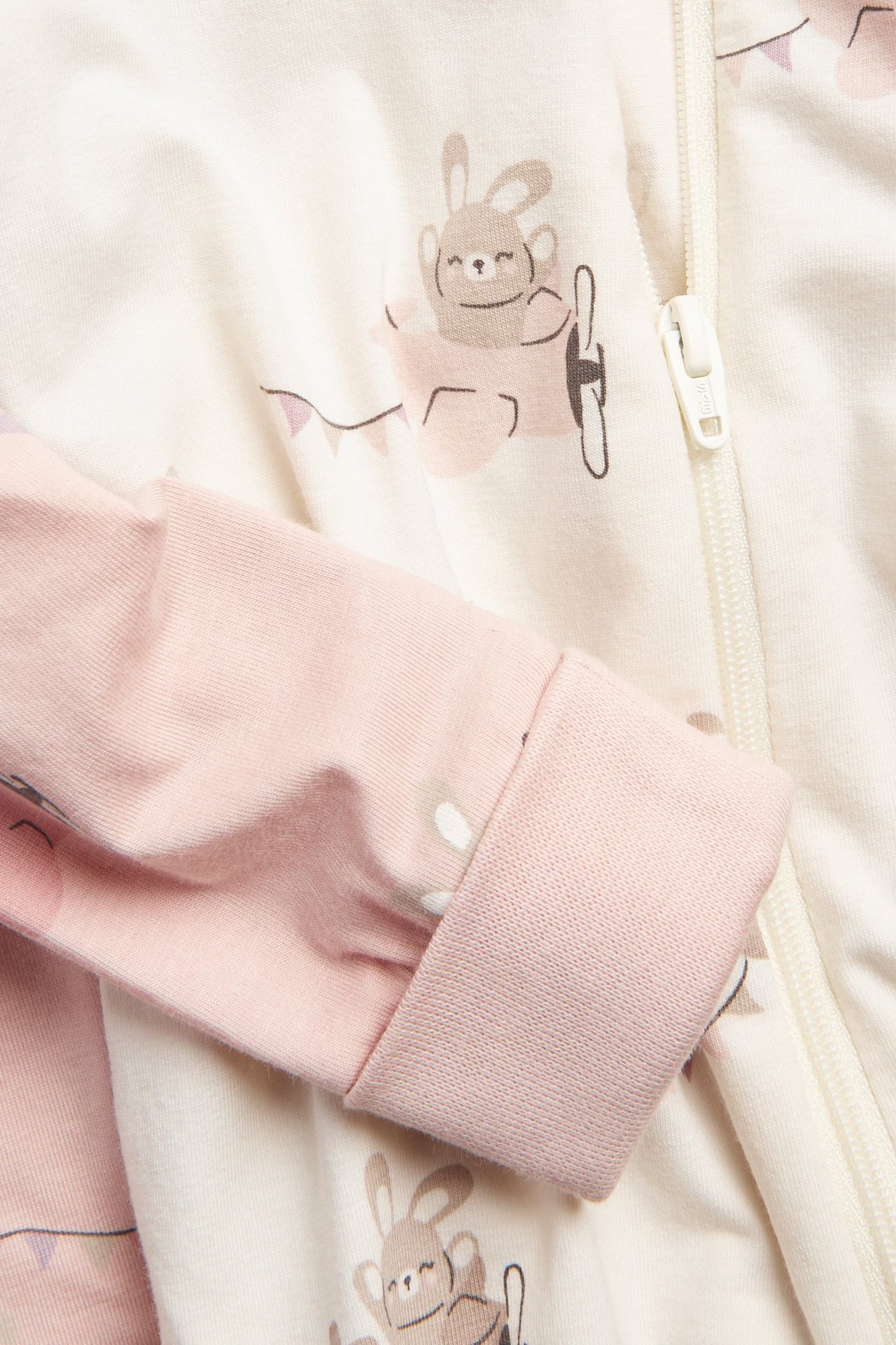 Nærbilde av en kremfarget baby-romper med rosa dyremønster, forlengede rosa mansjetter og toveis glidelås.