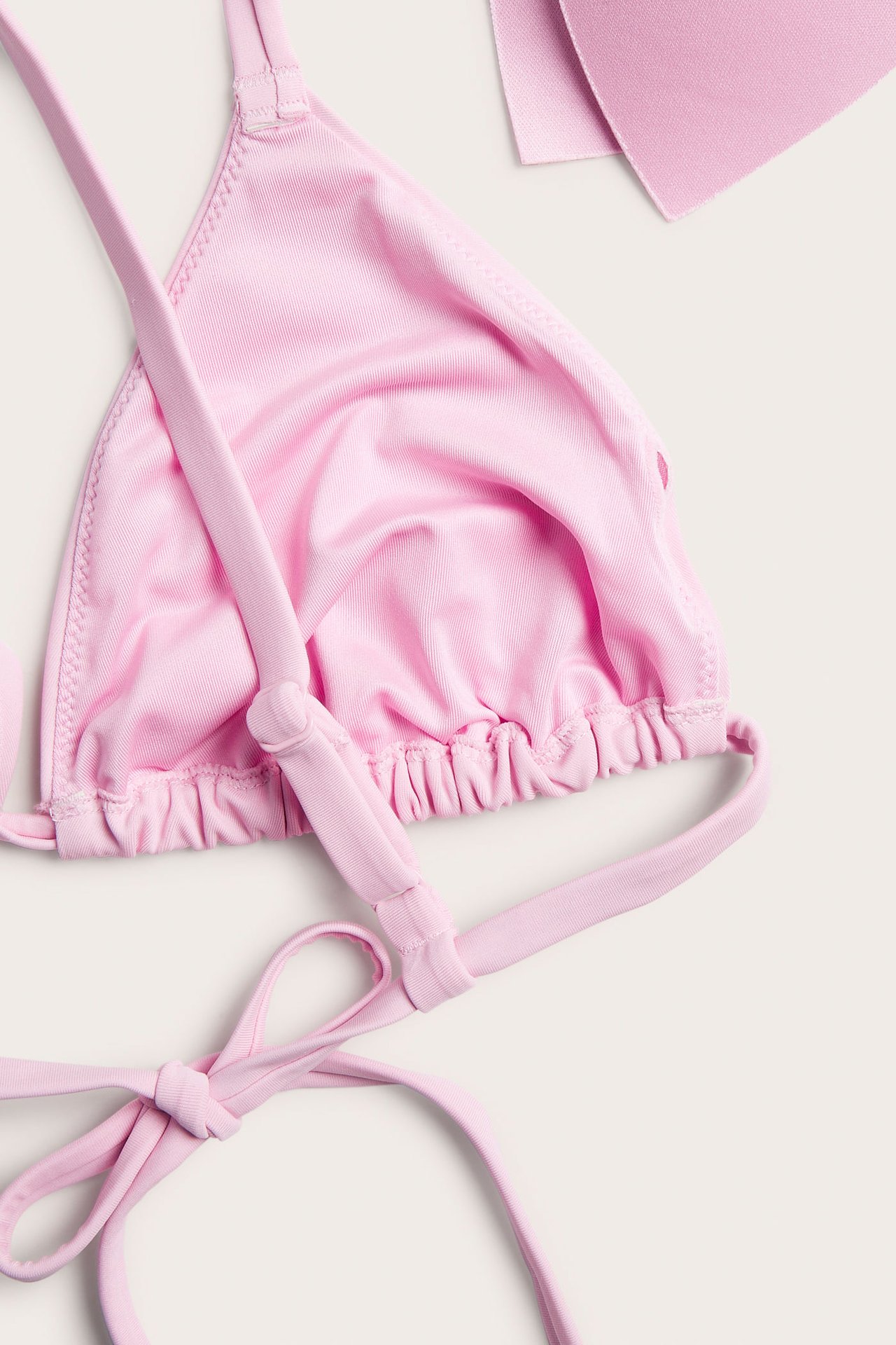 Närbild, uppifrån, av en rosa vadderad trekantsbikini-bh med knytband och rynkad underkant.