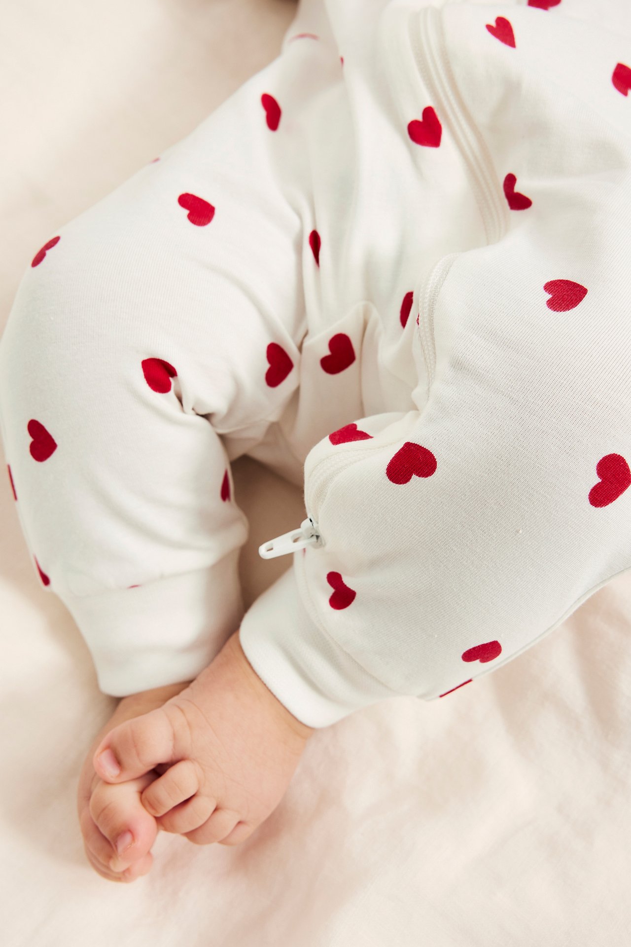 Lähikuva vauvan jaloista, yllään luonnonvalkoinen pyjama punaisilla sydämillä, valkoinen vetoketju.