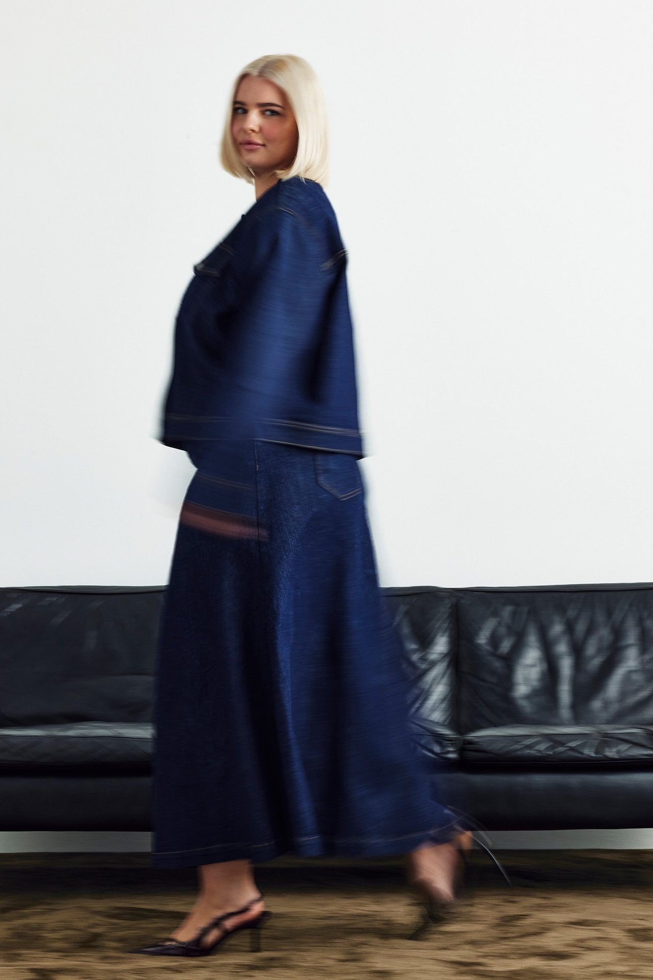 Sivukuva naisesta tummansinisessä A-linjaisessa farkkuhameessa, takissa ja mustissa sandaaleissa.