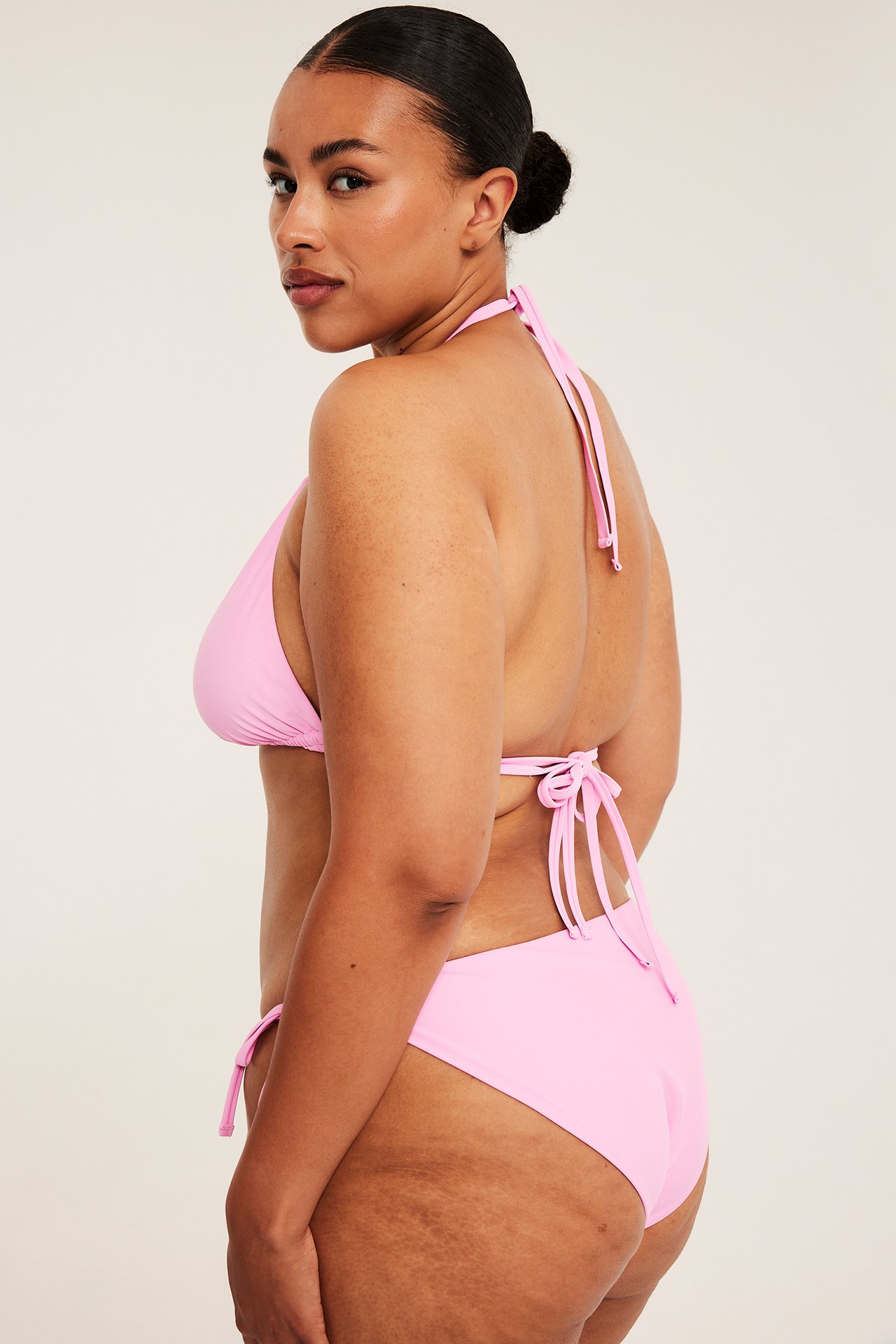 Sidovy av en kvinna i rosa halterneck bikinitopp och matchande bikiniunderdel med knytband.