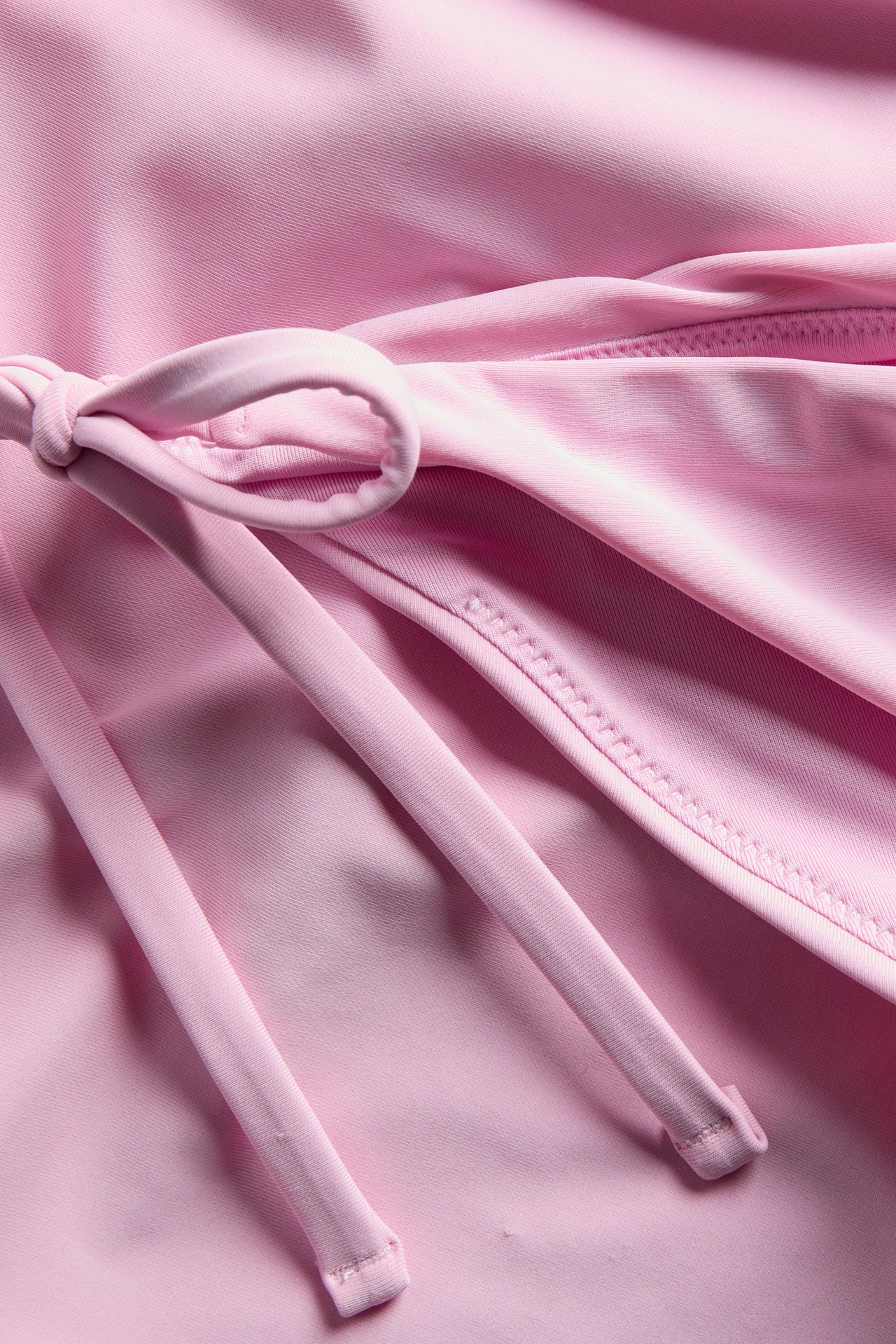 Närbild av en rosa bikinitrosa brief med knytband i sidan, som visar slätt, enfärgat tyg.