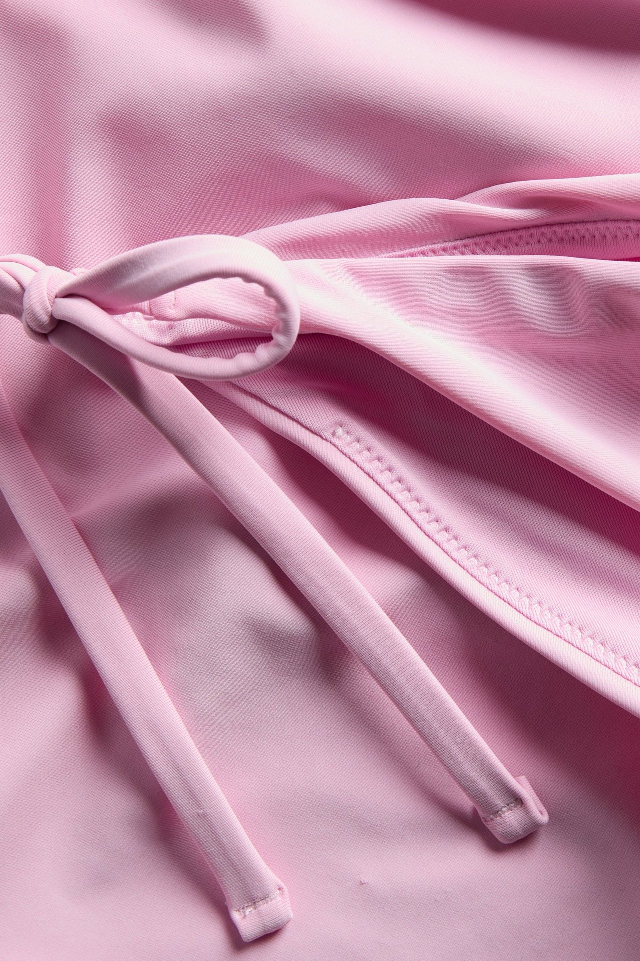 Nærbilde av en rosa bikinitruse med knytebånd i siden, som viser glatt, ensfarget stoff.