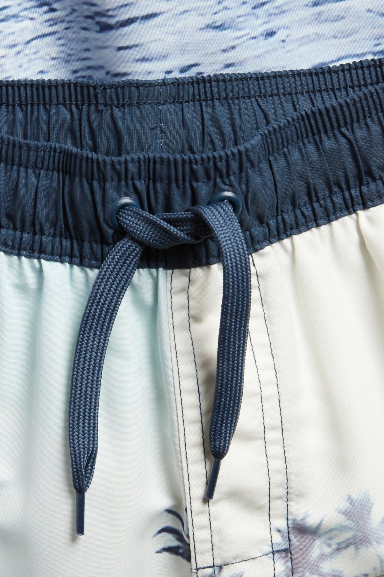 Szorty kąpielowe dziecięce: granatowa gumka, sznurek i jasnoniebiesko-biały fotonadruk.