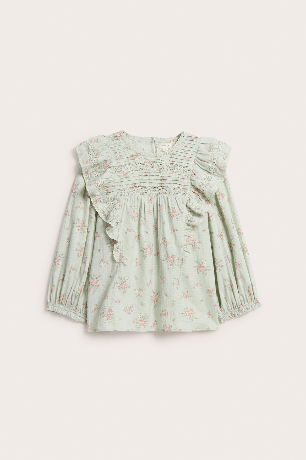 Widok z przodu jasnej zielonej kwiecistej bluzki bawełnianej z koronkowymi falbanami, plisami i rękawami 3/4.