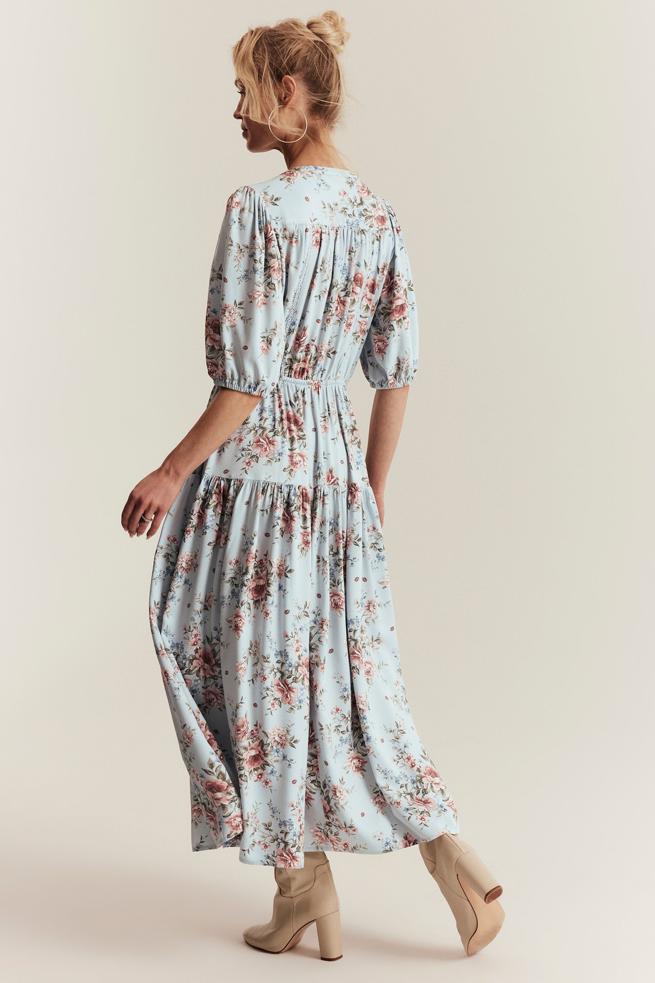 Baksidebilde av en kvinne i en lyseblå blomstret viskosemaxikjole og lysebeige ankelstøvletter.