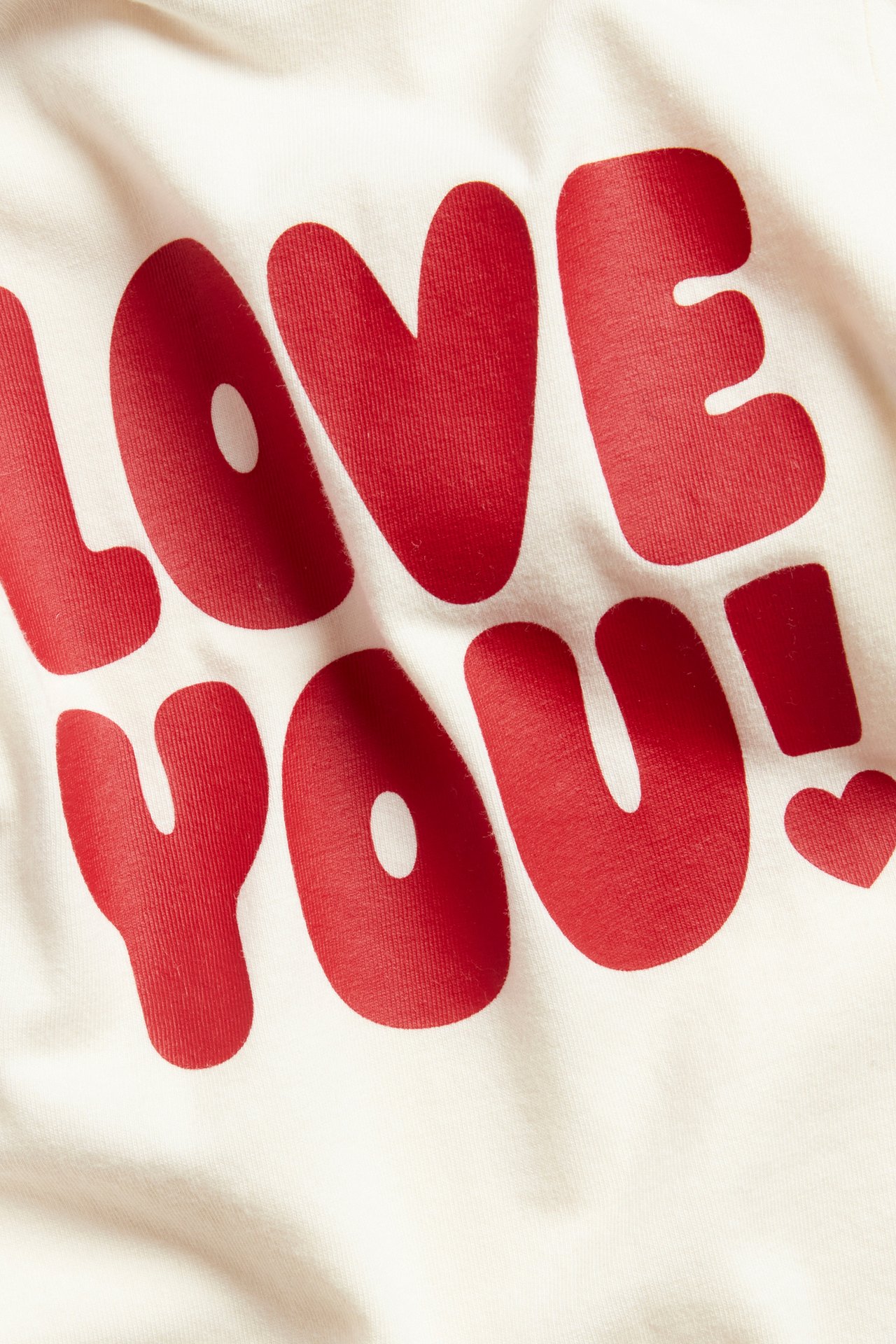 Nærbilde av en offwhite langermet babybody med rødt 'LOVE YOU!'-trykk.