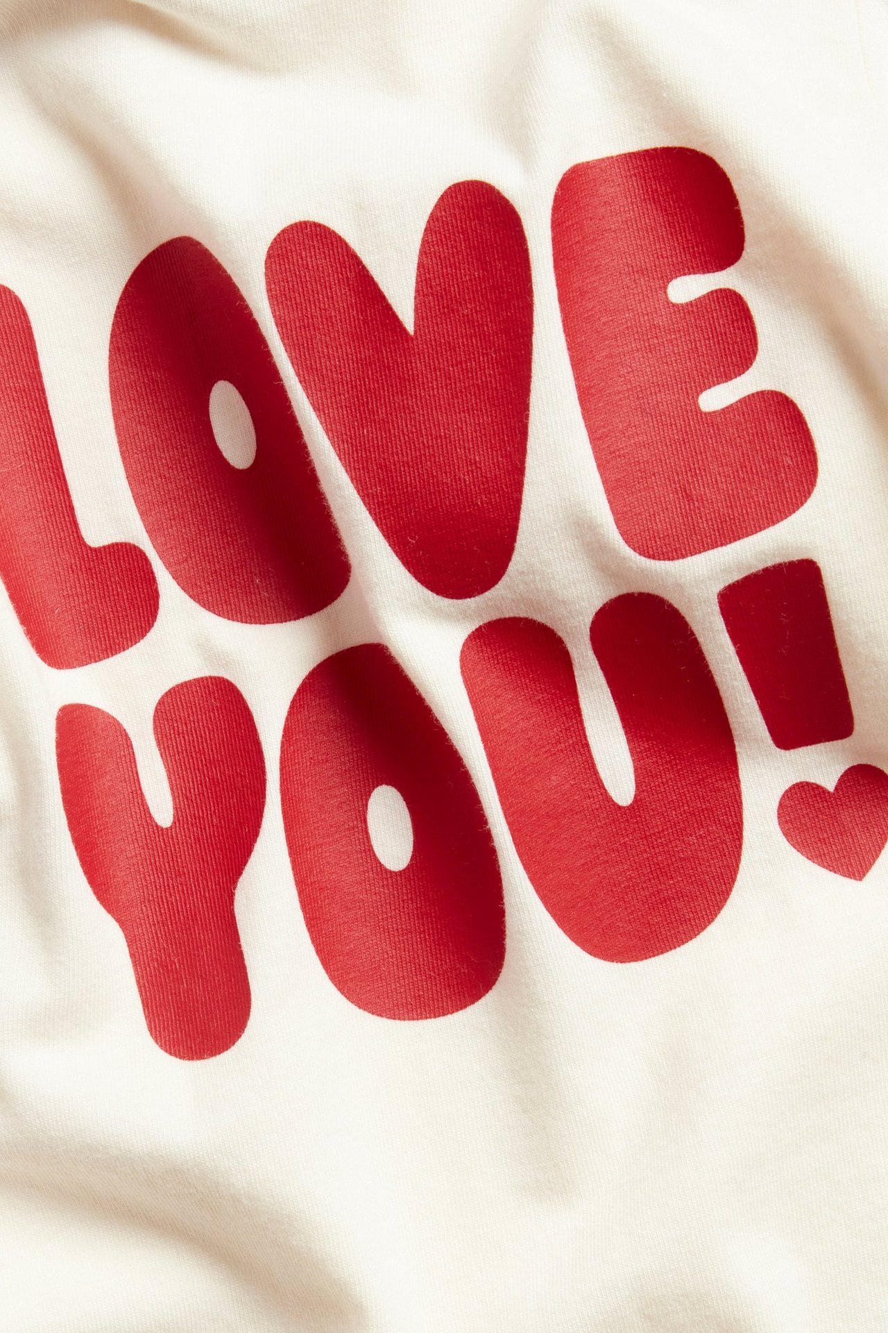 Zbliżenie na ecru body niemowlęce z długim rękawem z czerwonym nadrukiem 'LOVE YOU!'.