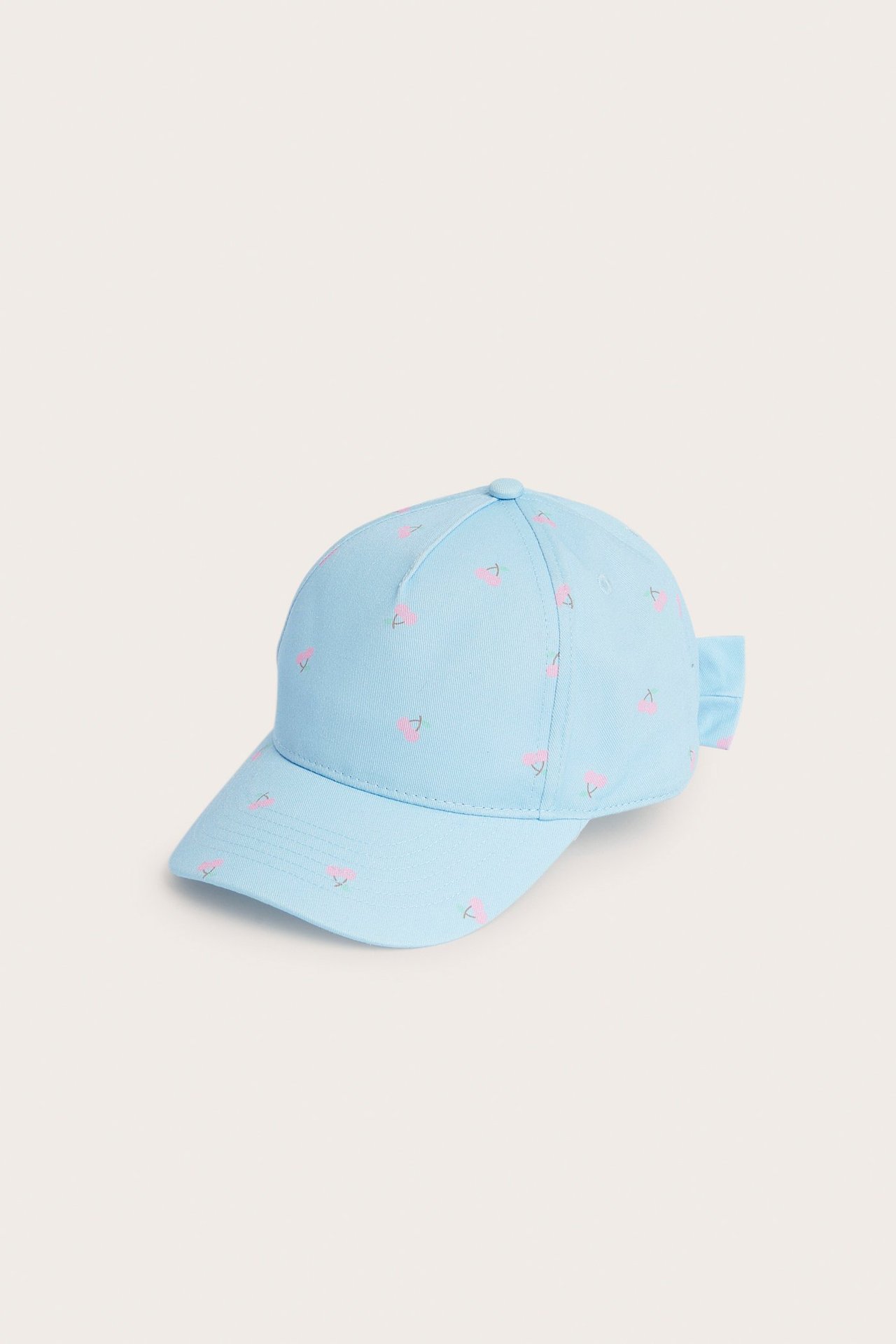 Edestä ja sivulta vaaleansininen lasten lippalakki kirsikkakuviolla ja pienellä rusetilla takana.