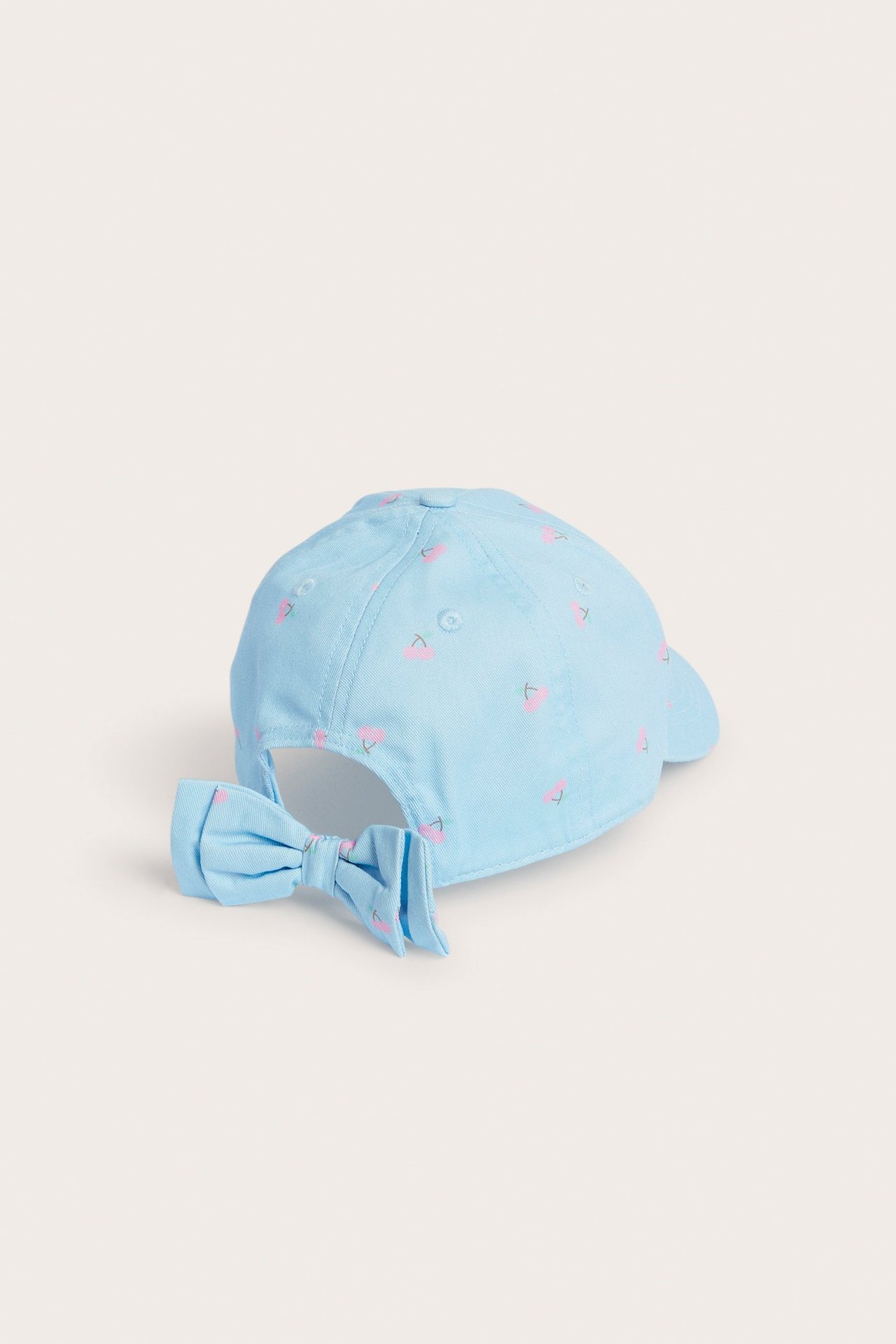 Takaapäin vaaleansininen lasten lippalakki kirsikkakuviolla ja yhteensopivalla rusetilla.