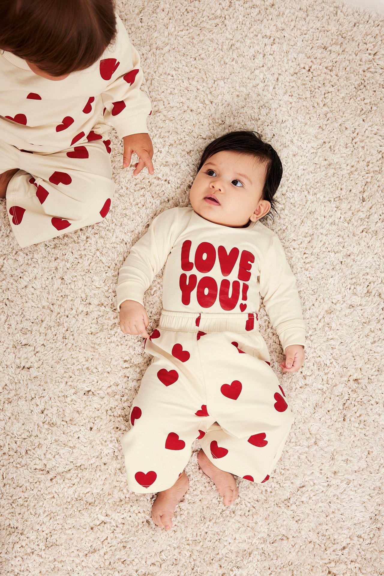 Ovenfra: baby i offwhite joggebukse med røde hjerter og matchende 'LOVE YOU!'-topp.