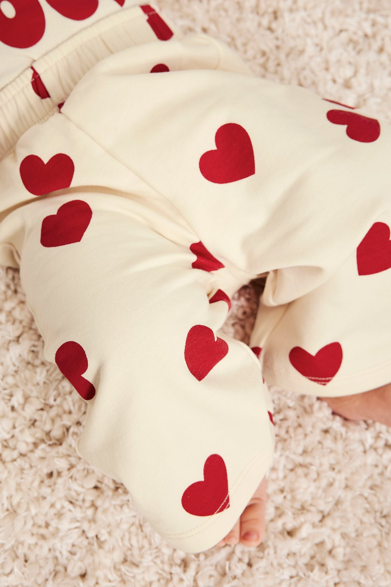 Lähikuva vauvan jaloista kermanvärisissä suorissa collegehousuissa punaisella sydänkuviolla.