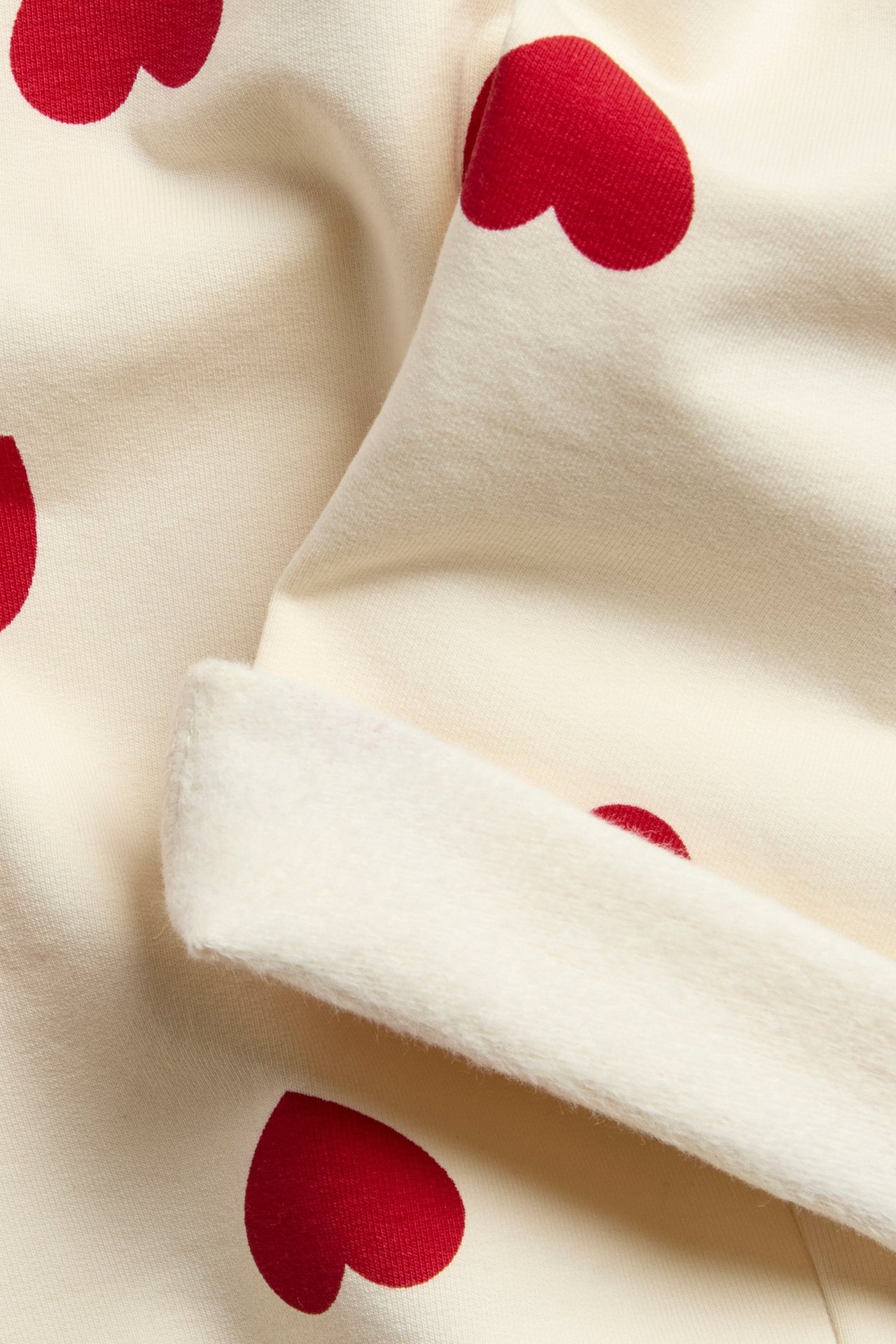 Lähikuva vauvan luonnonvalkoisista collegehousuista, joissa on punaisia sydänkuvioita.