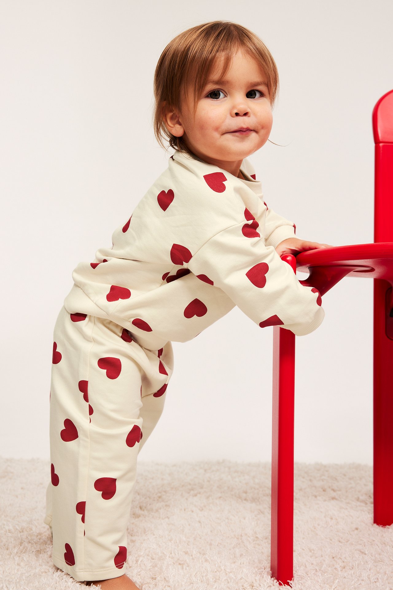 Vauva edestä: Luonnonvalkoiset verryttelyhousut punaisilla sydämillä ja niihin sopiva pusero.