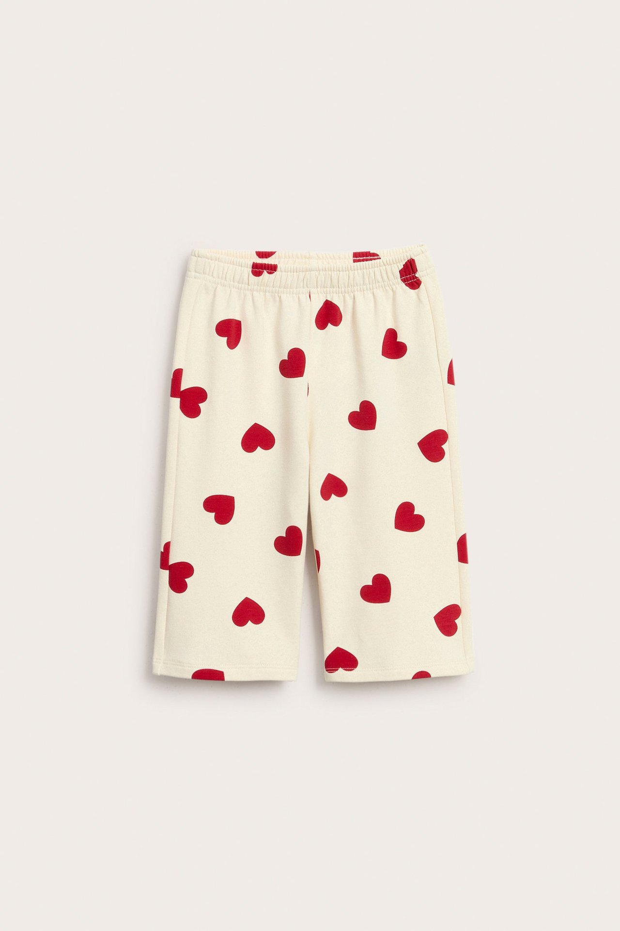 Edestä kuvatut luonnonvalkoiset vauvan collegeshortsit punaisella sydänkuviolla, joustava vyötärö.