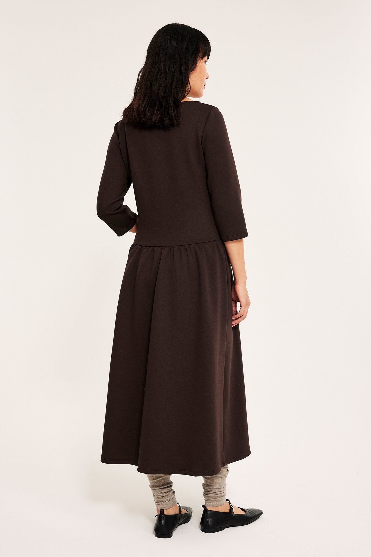 Naise on tummanruskea jersey midimekko sivutaskuilla, takanäkymä.