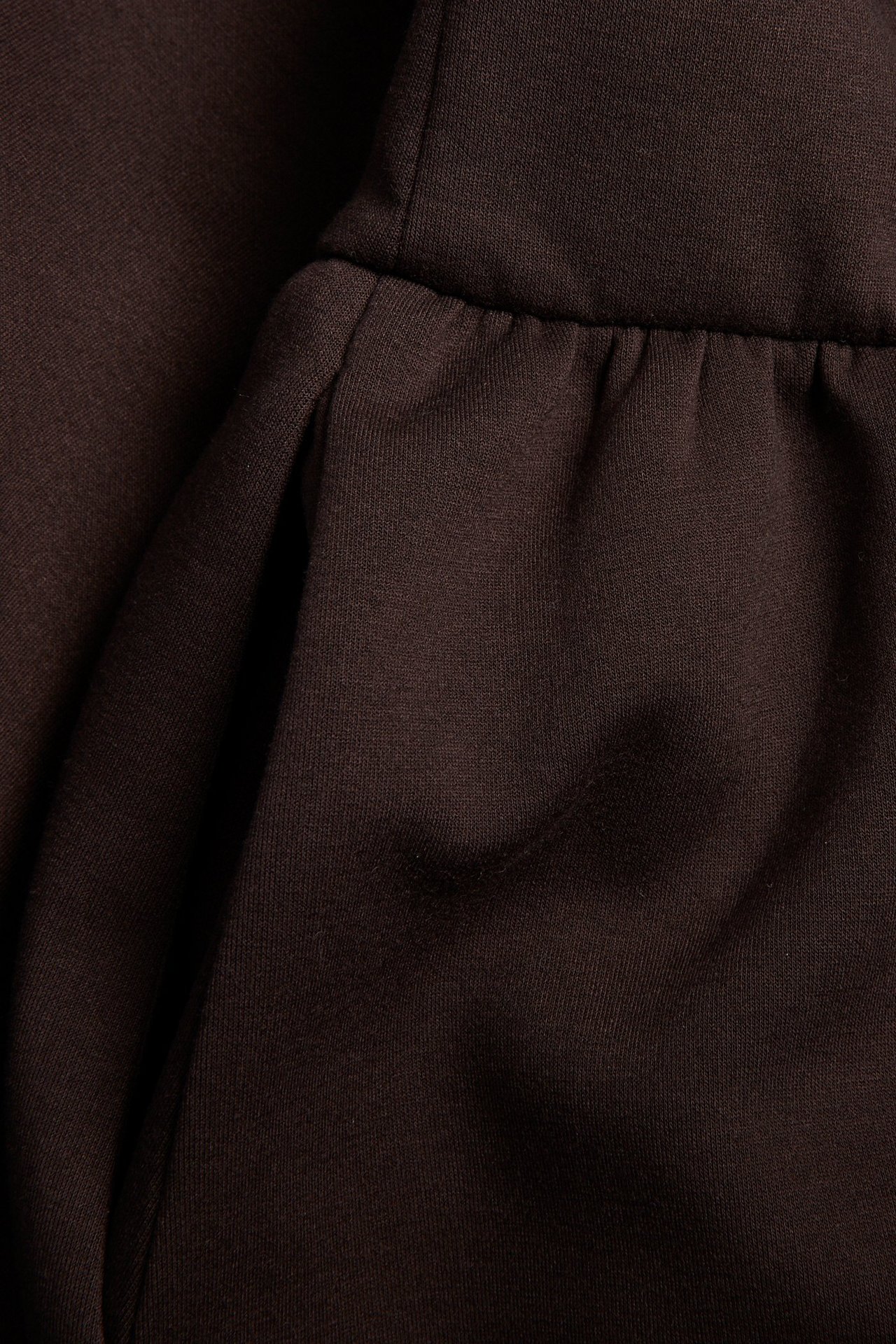 Zbliżenie na ciemnobrązową sukienkę dżersejową fasonu fit & flare ze marszczonymi detalami.
