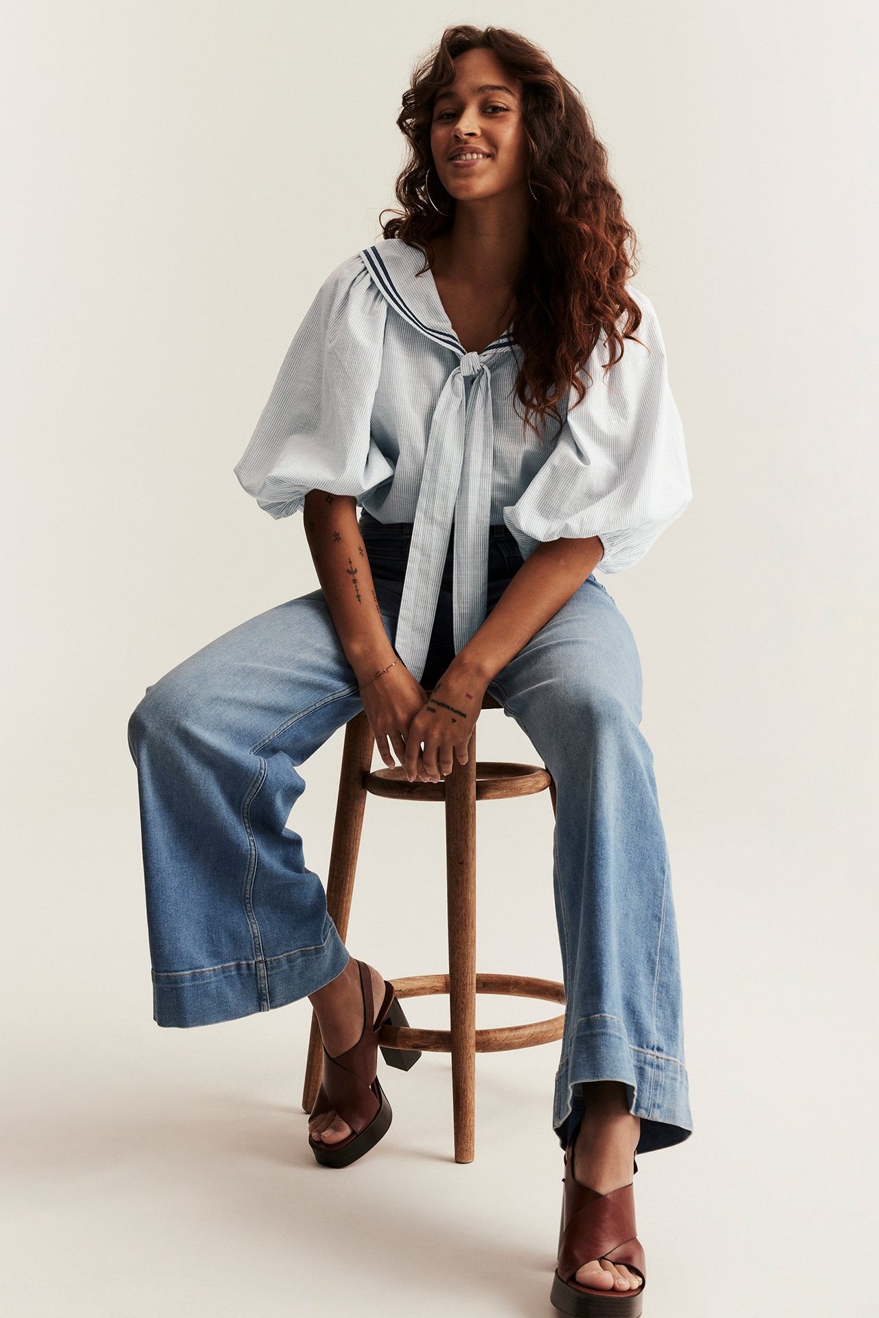 Nainen edestä: raidallinen merimiespusero puffihihoilla, leveälahkeiset farkut ja ruskeat platform-sandaalit.