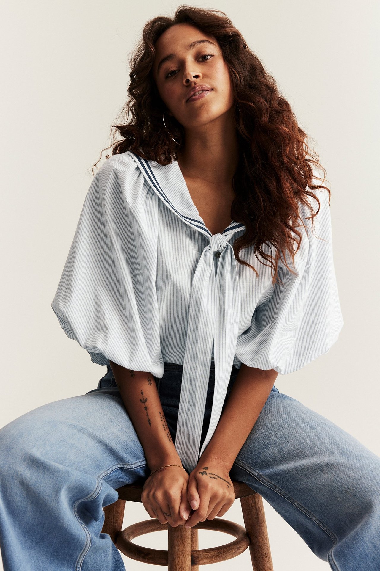 Widok z przodu: Kobieta w niebieskiej bluzce w paski, bufiastymi rękawami, wiązaniem pod szyją i jasnoniebieskich dżinsach.