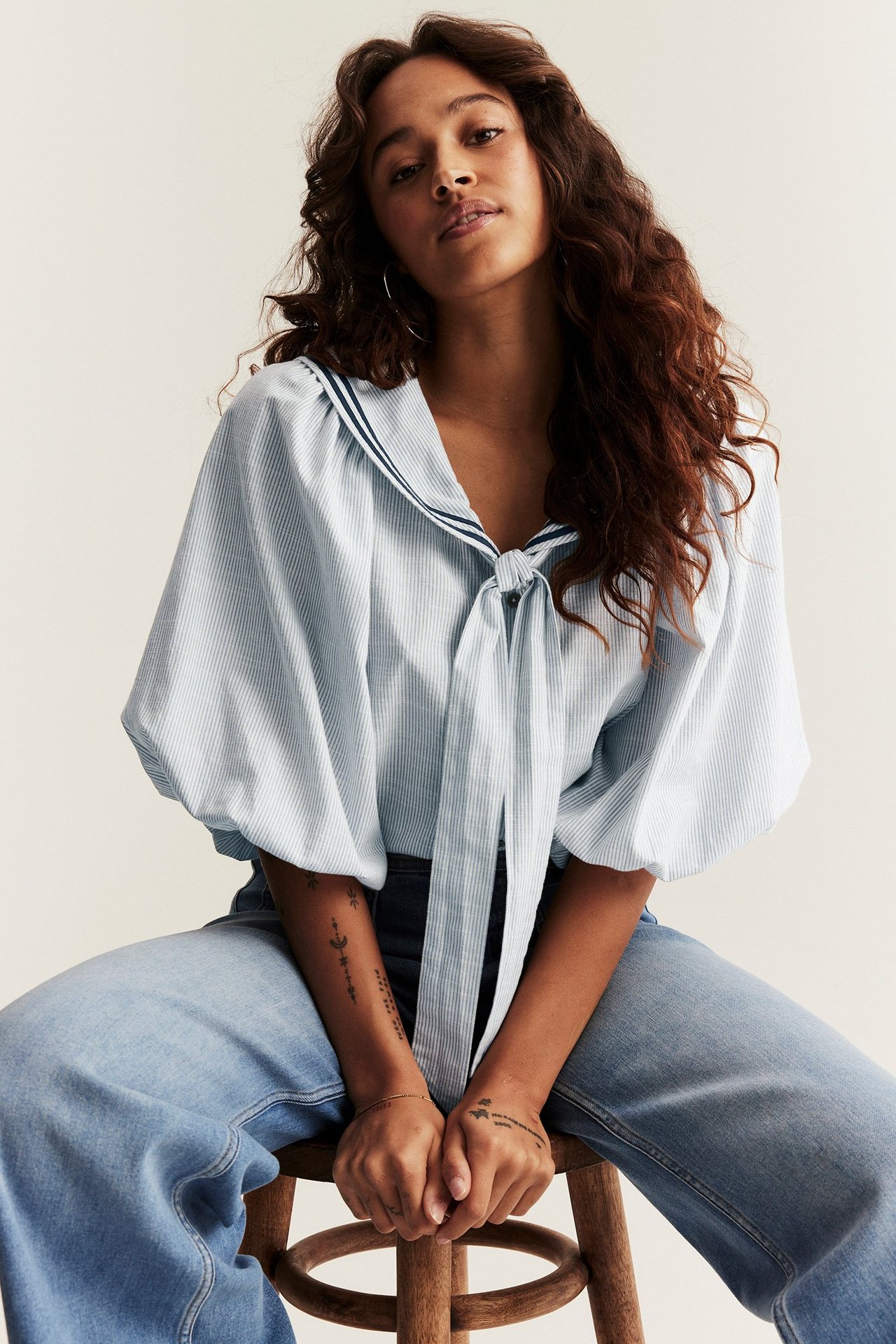 Nainen edestä: vaaleansininen raidallinen merimiespusero puhvihihoilla ja rusetilla, farkkujen kanssa.