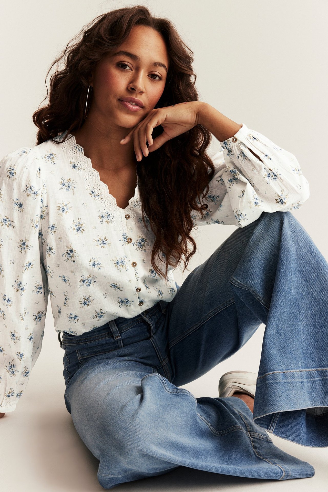 Kvinne i offwhite blomstret bluse med brodert V-hals, puffermer og blå jeans.