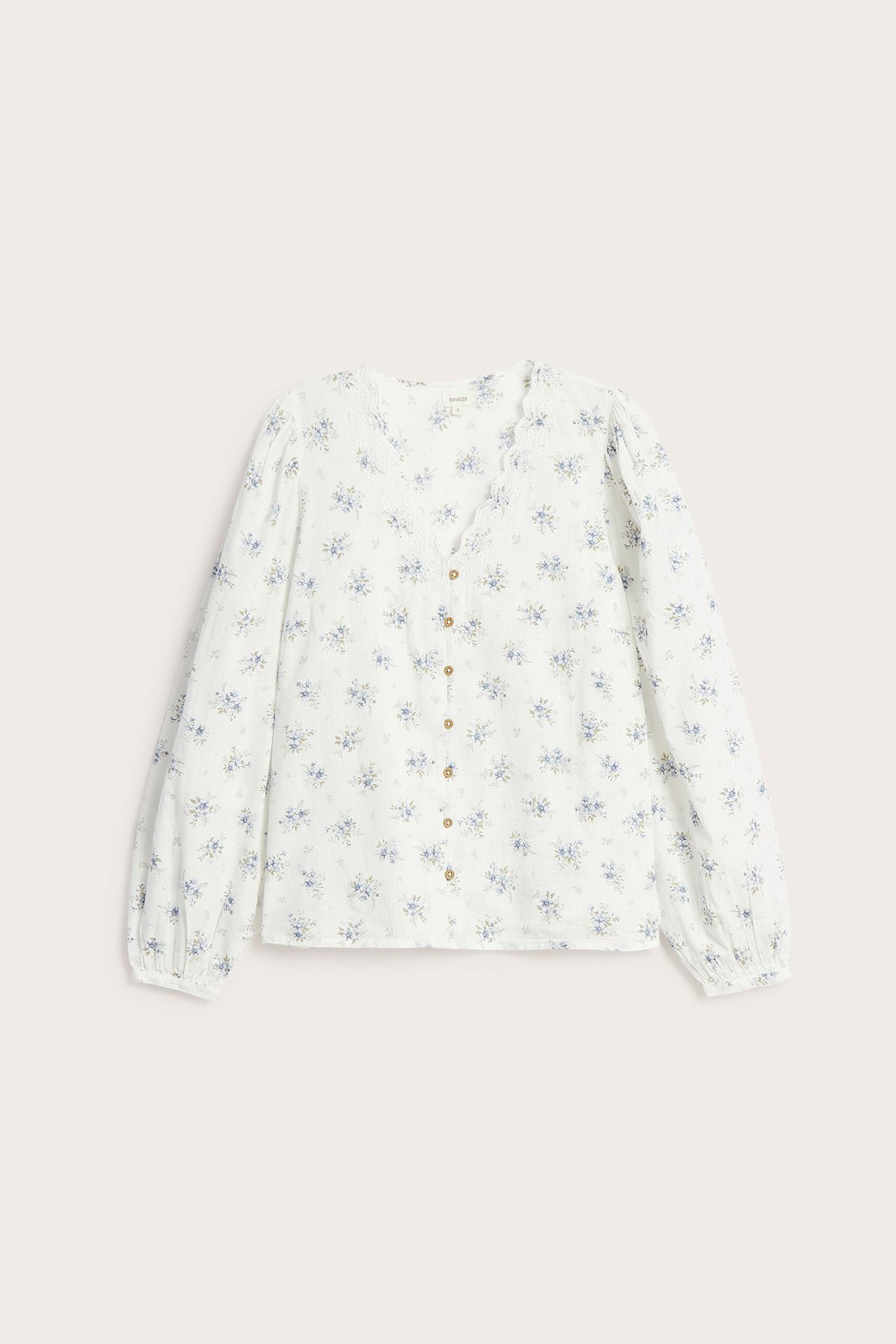 Forfra: Offwhite bomullsbluse med småblomstret mønster, brodert V-hals, puffermer og tildekkede knapper.