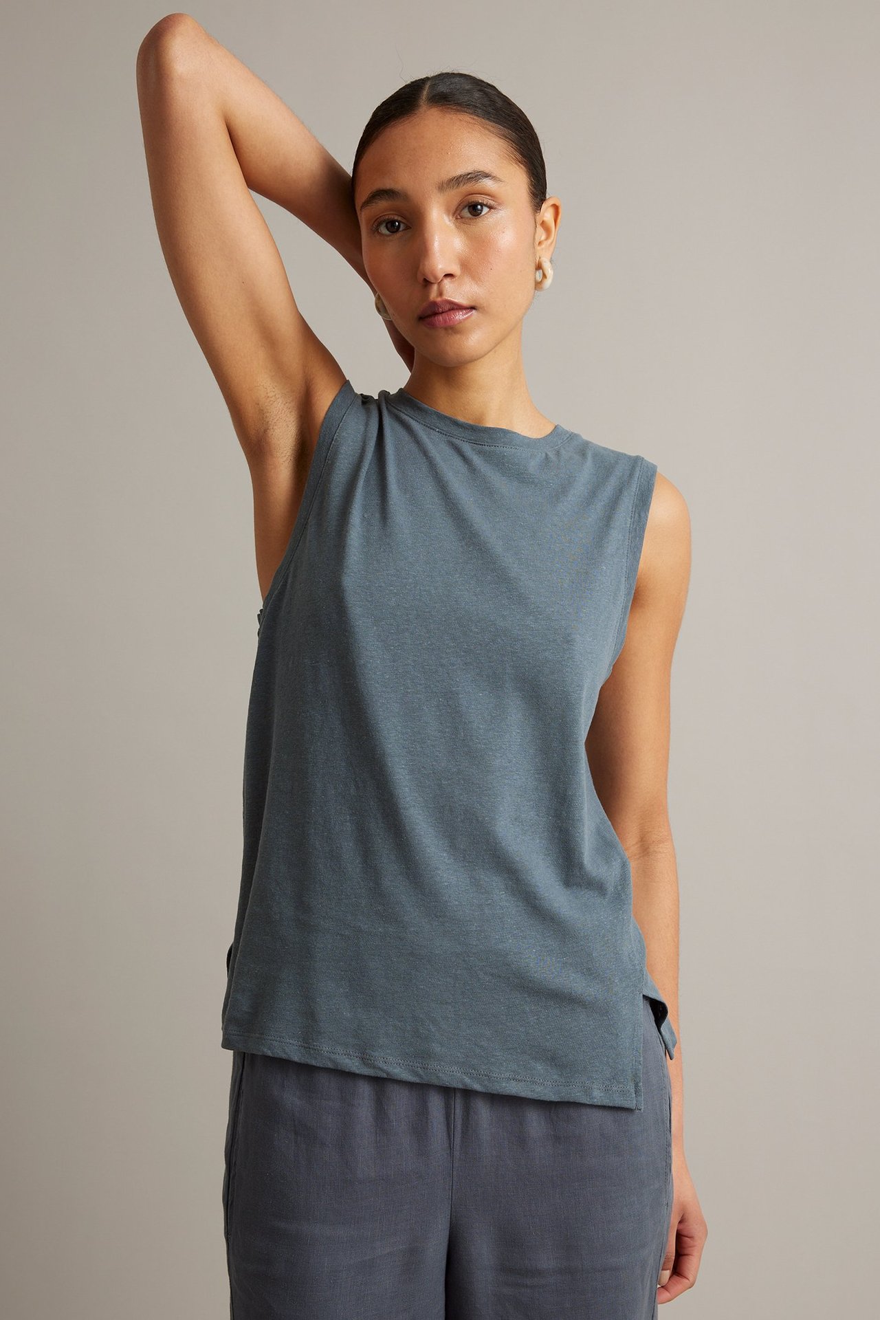 Widok z przodu: kobieta w niebieskim topie z lnu i bawełny, granatowych kulotach, jasnych kolczykach.