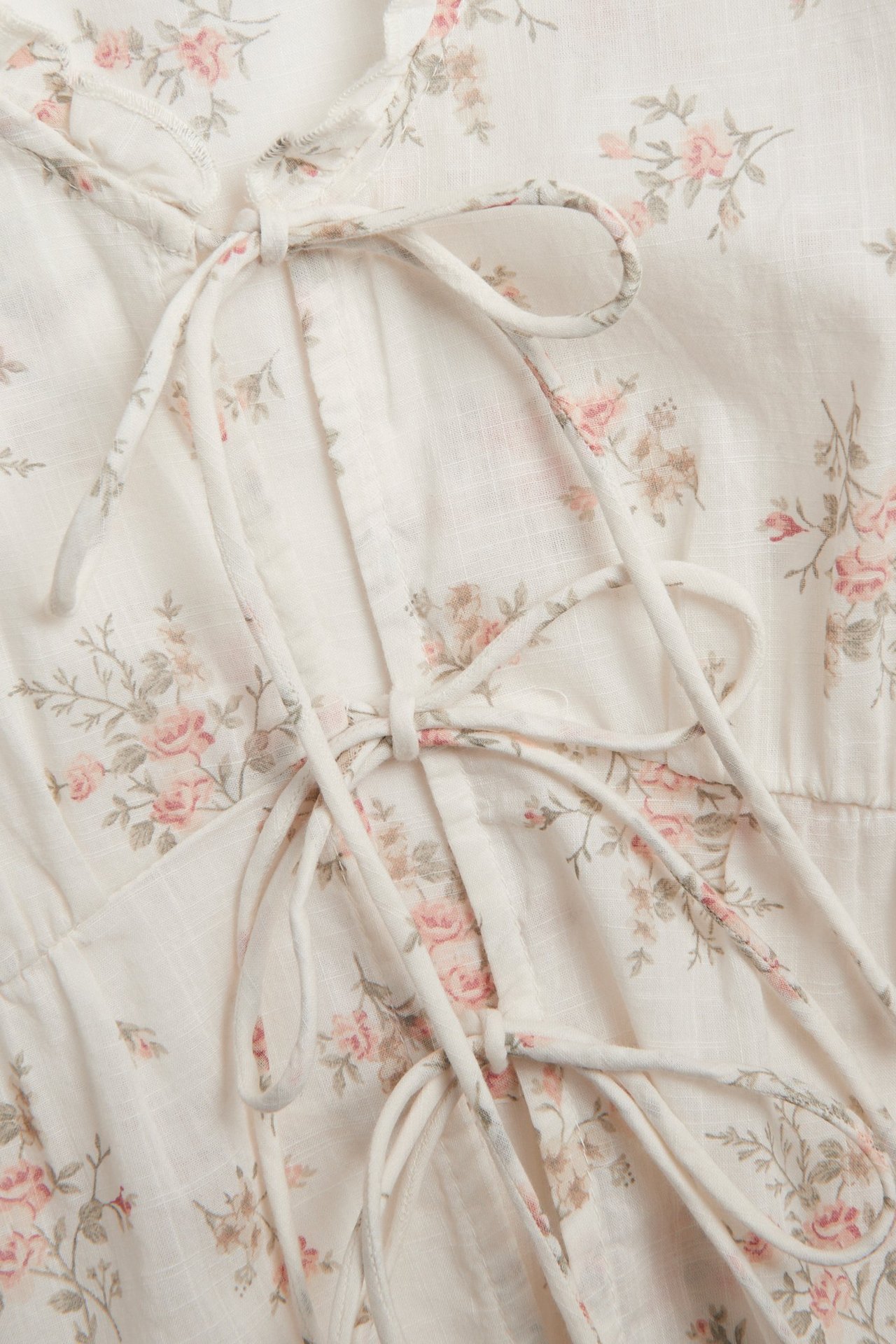 Nærbilde forfra av en off-white bomullsbluse med rosa blomstermønster og knytebånd foran.